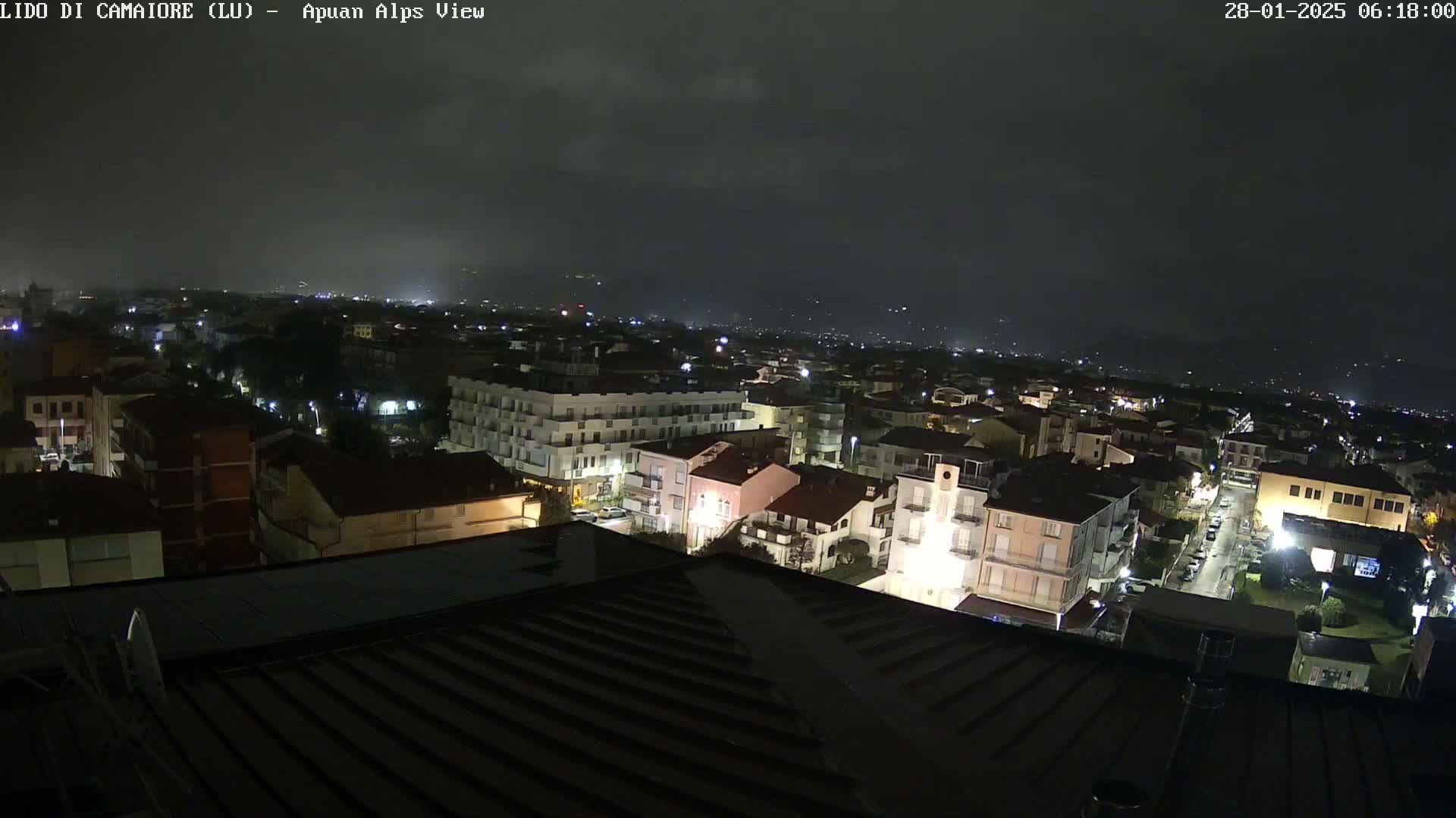 A nighttime, overcast view of a town with many buildings lit up, seen from a rooftop.