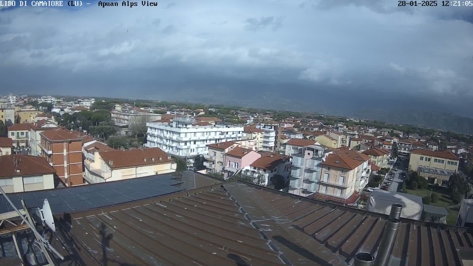 A cloudy day overlooking a town of low-rise buildings with red-tiled roofs, viewed from a rooftop with solar panels.