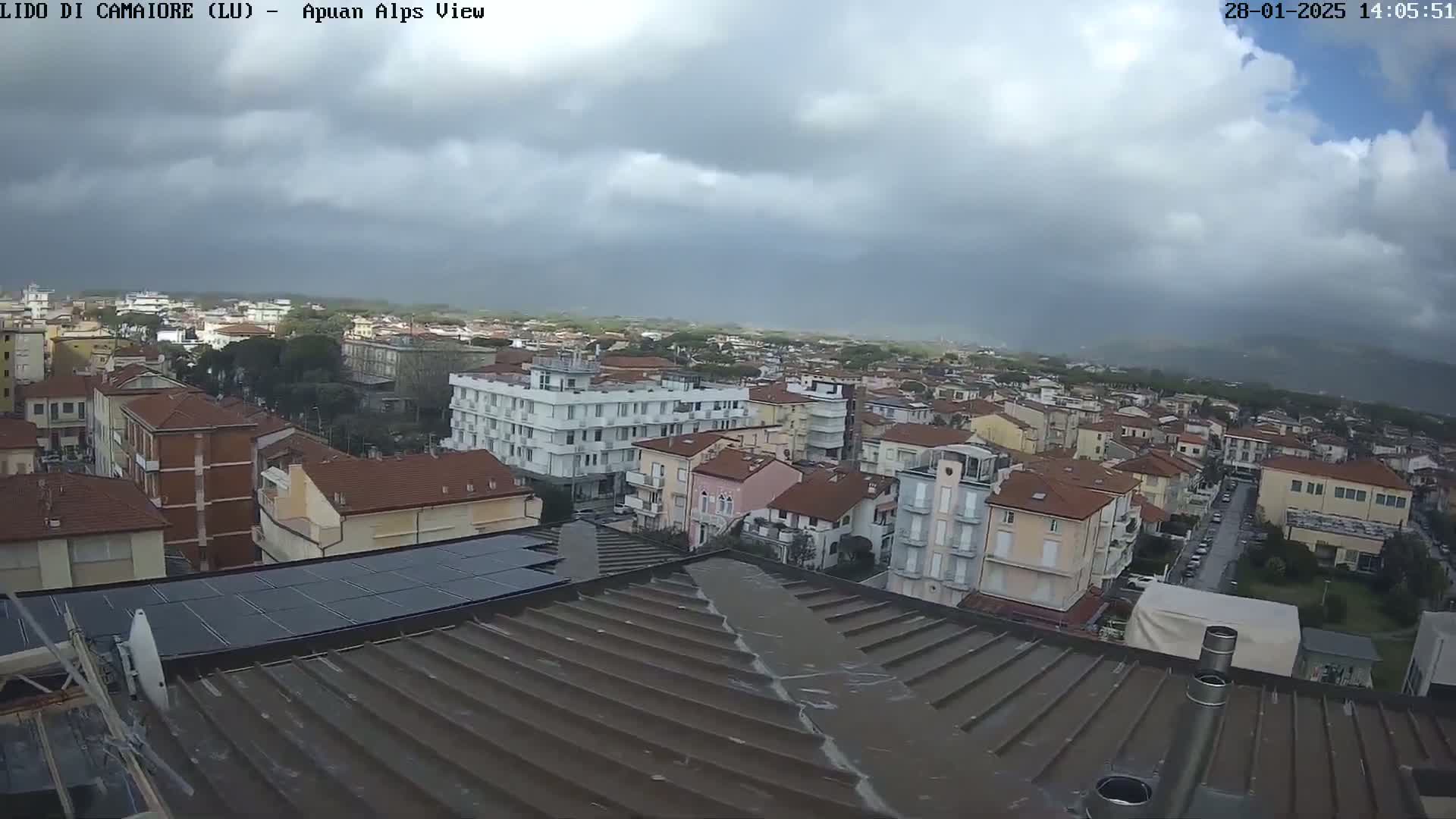 A view from a rooftop shows a town under a cloudy sky, with some rain possibly falling.