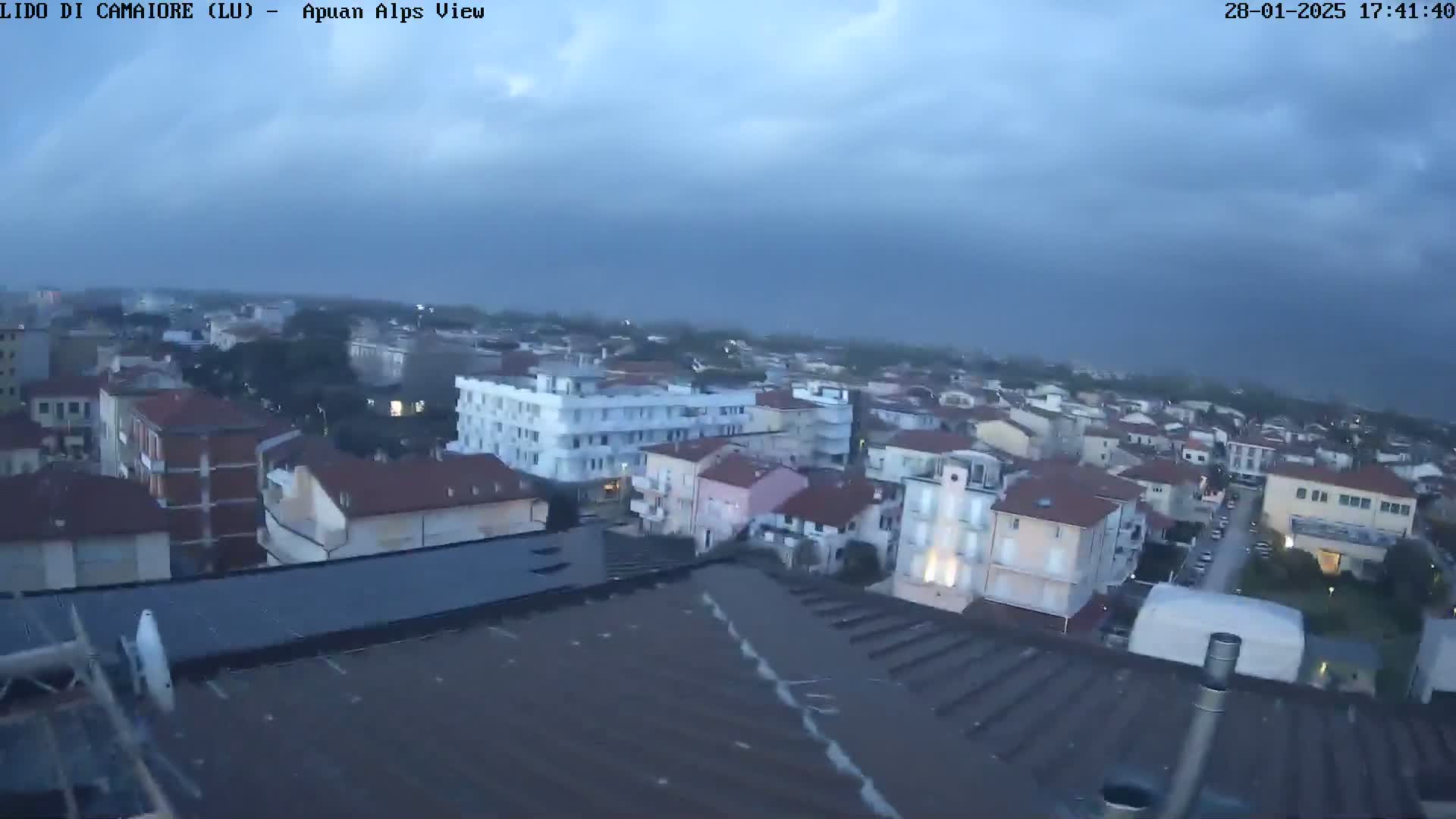 A high-angle, long shot shows a town under a cloudy, overcast sky.