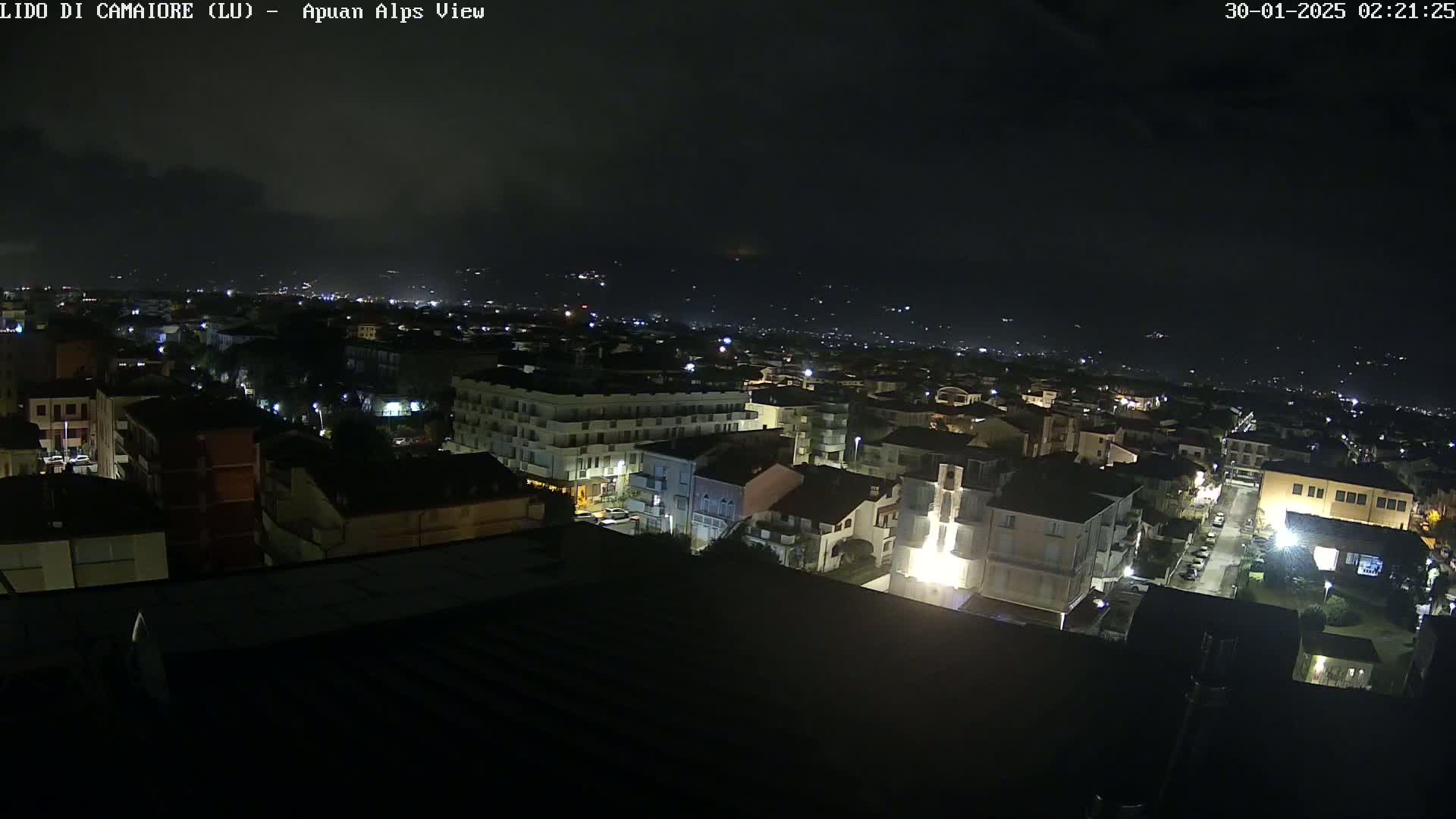 A nighttime, high-angle view of a town with dimly lit buildings under a dark, cloudy sky.