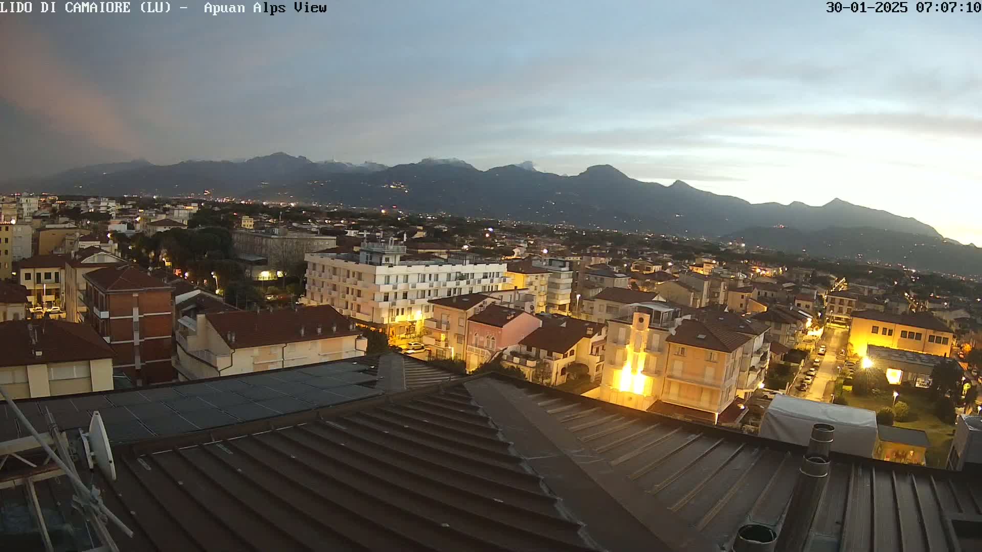 A nighttime view of a town nestled at the base of a mountain range under a twilight sky.