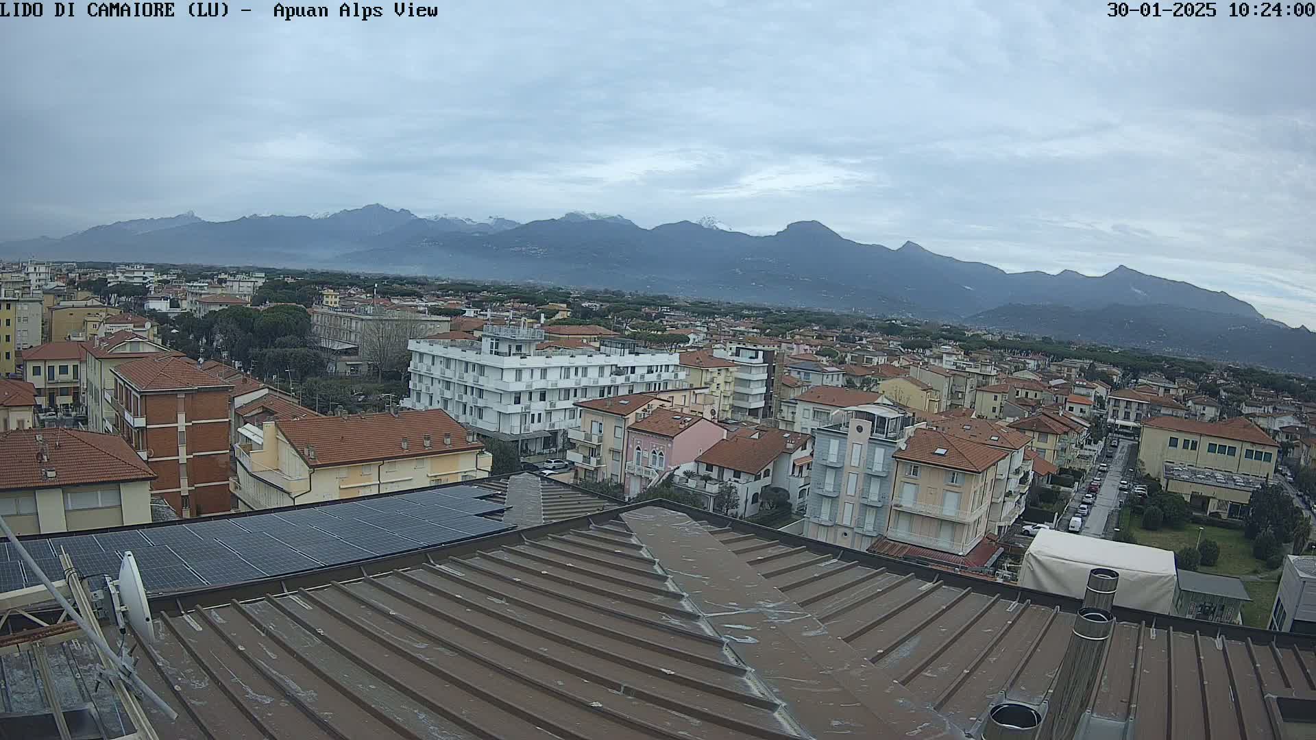 A view from a rooftop shows a town under an overcast sky with snow-capped mountains in the distance.