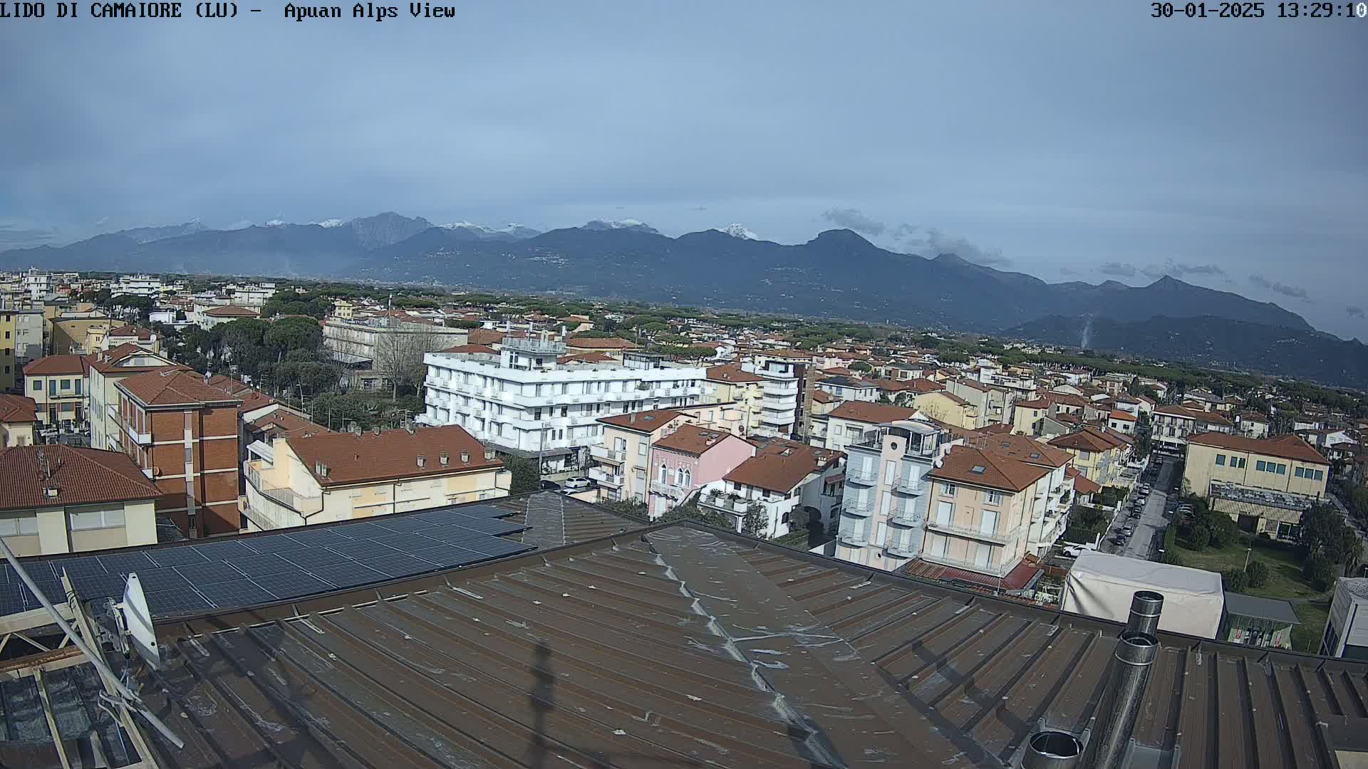 A rooftop view of a town nestled beneath snow-capped mountains on a mostly clear day.