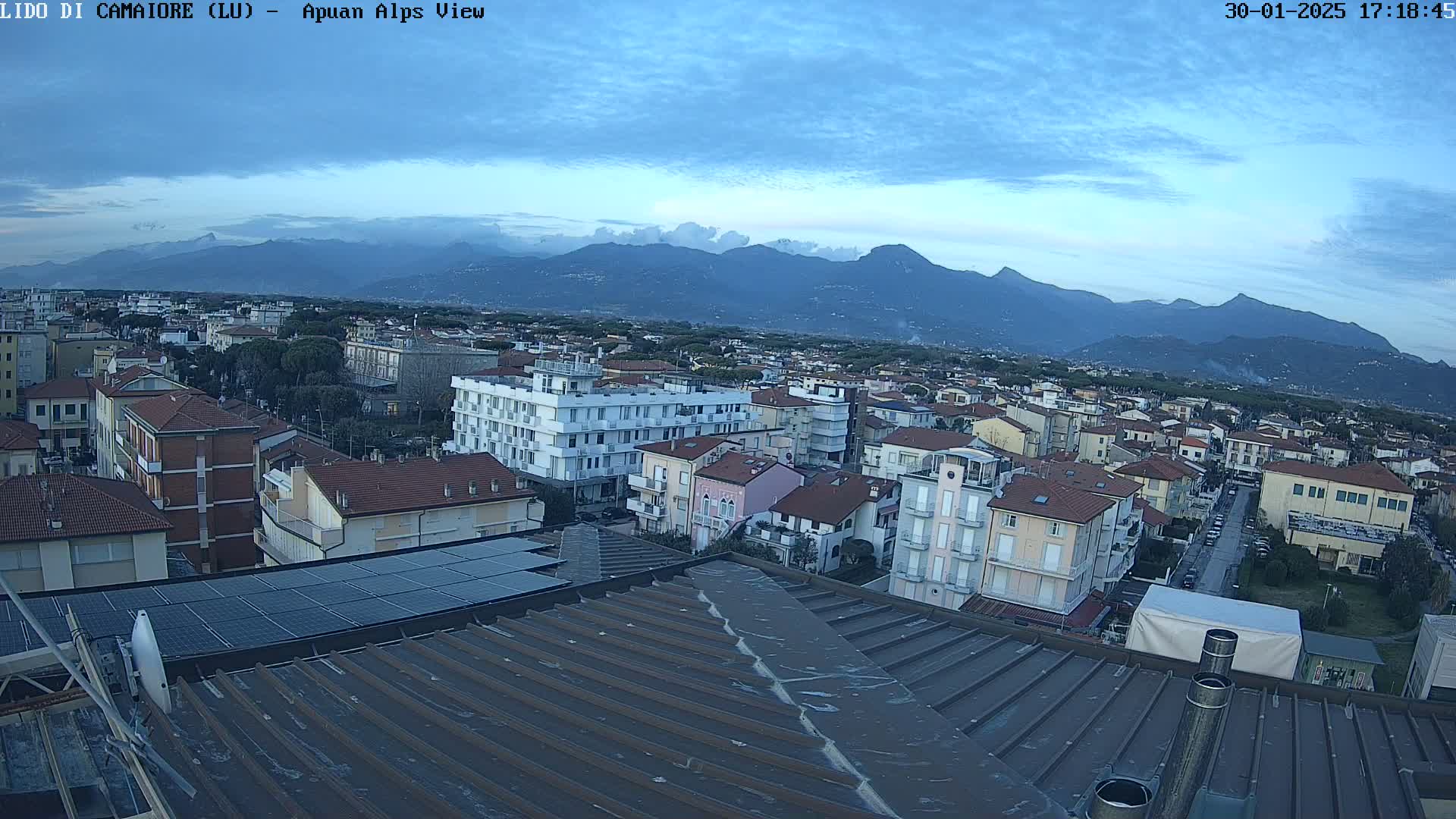 A mostly cloudy, twilight view overlooking a town and distant mountains.