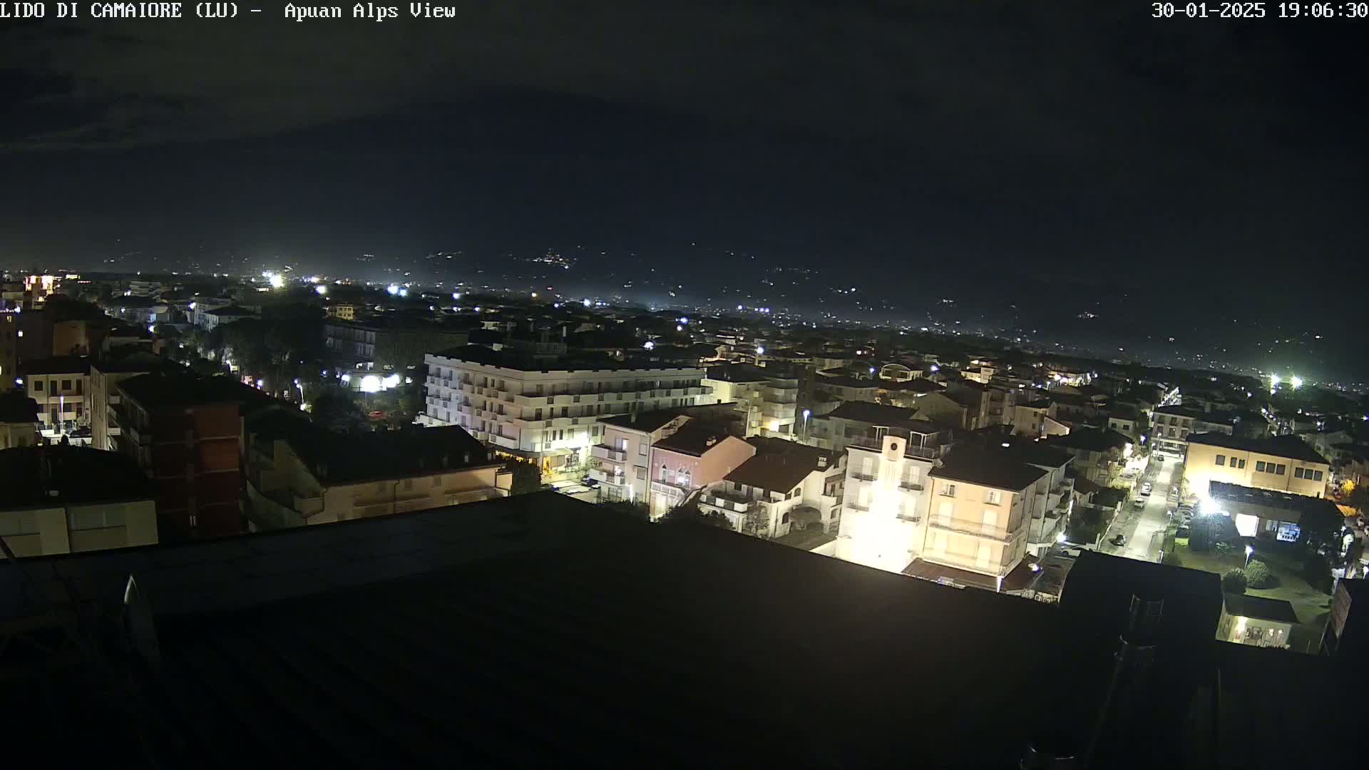 A nighttime, aerial view of a town illuminated by streetlights, with a mountain range faintly visible in the background under a clear, dark sky.