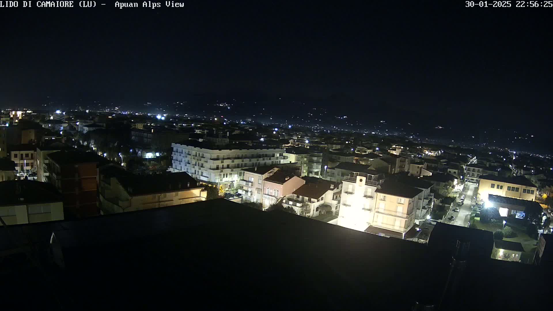 A nighttime, aerial view of a town, with distant hills faintly visible under a dark sky.