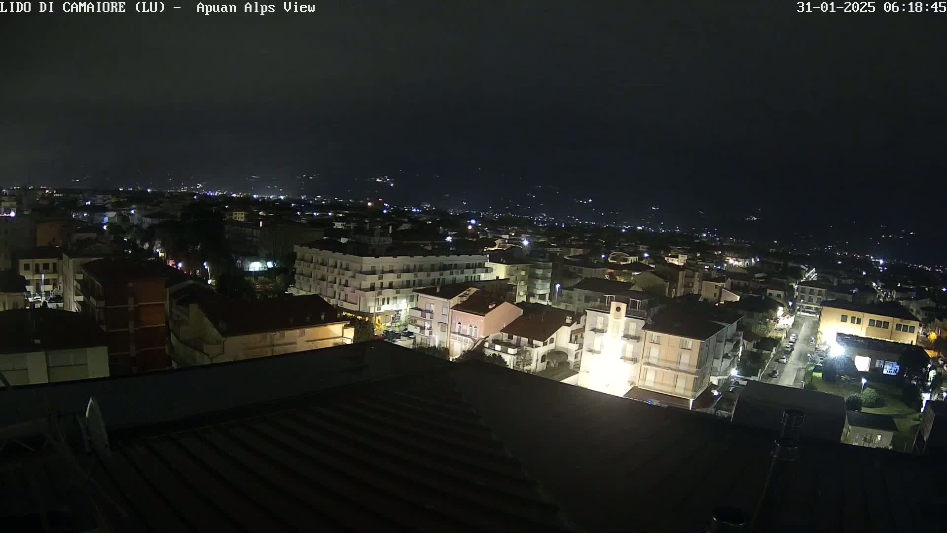 A nighttime aerial view of a town shows many buildings with illuminated windows under a dark, clear sky.