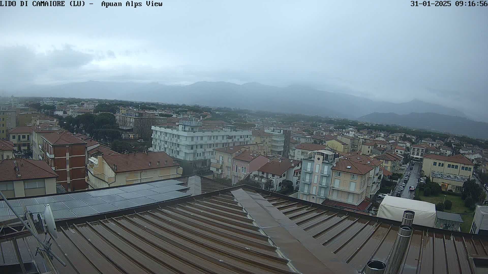 A rain-slicked rooftop overlooks a town nestled against a hazy mountain range under an overcast sky.