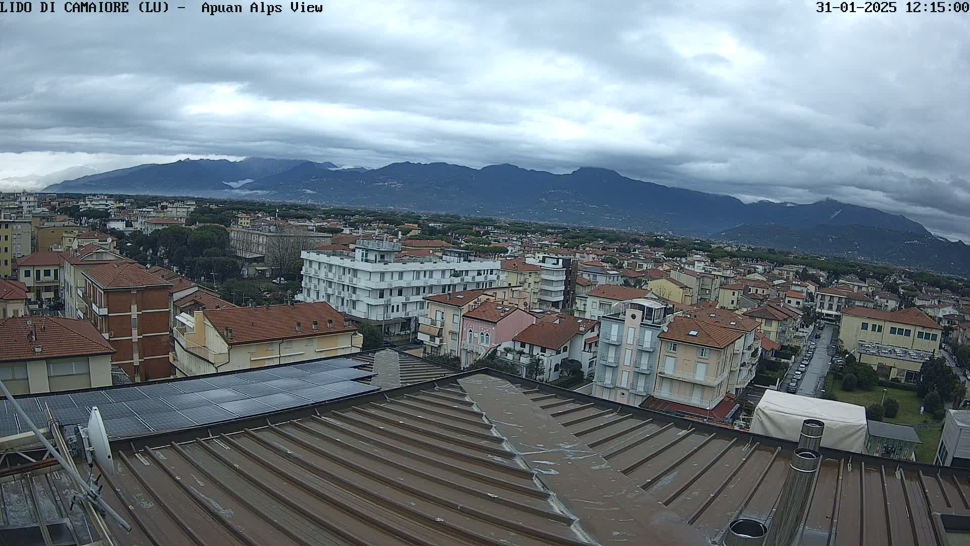 A view from a rooftop shows a town under a cloudy sky, with mountains in the distance.