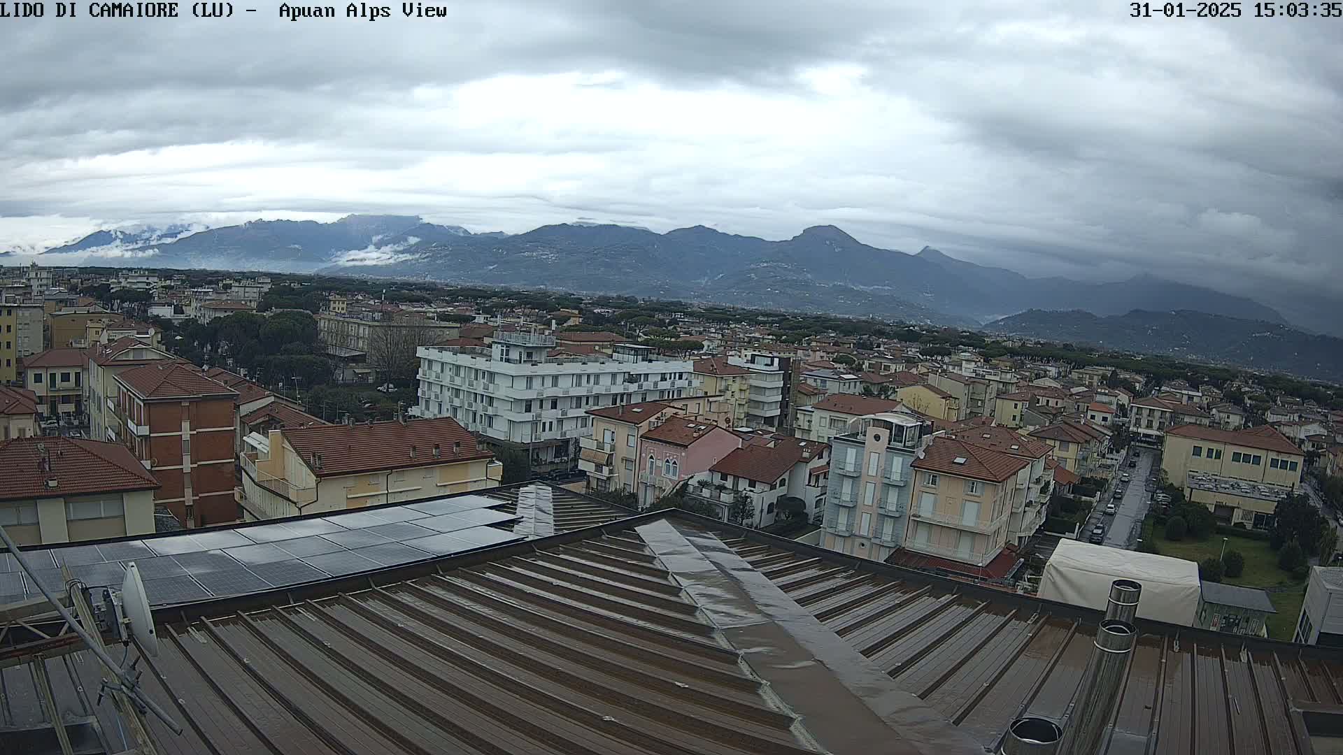 A wet rooftop overlooks a town nestled beneath overcast skies and a distant mountain range.