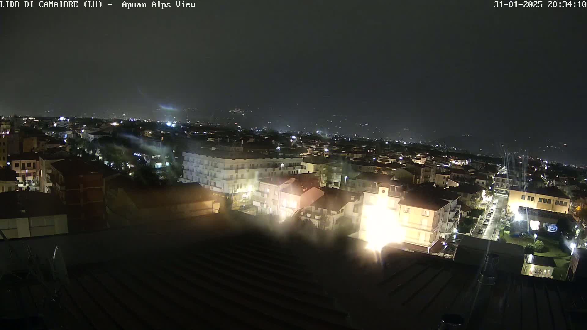 A nighttime aerial view of a town illuminated by streetlights and building lights under hazy conditions.