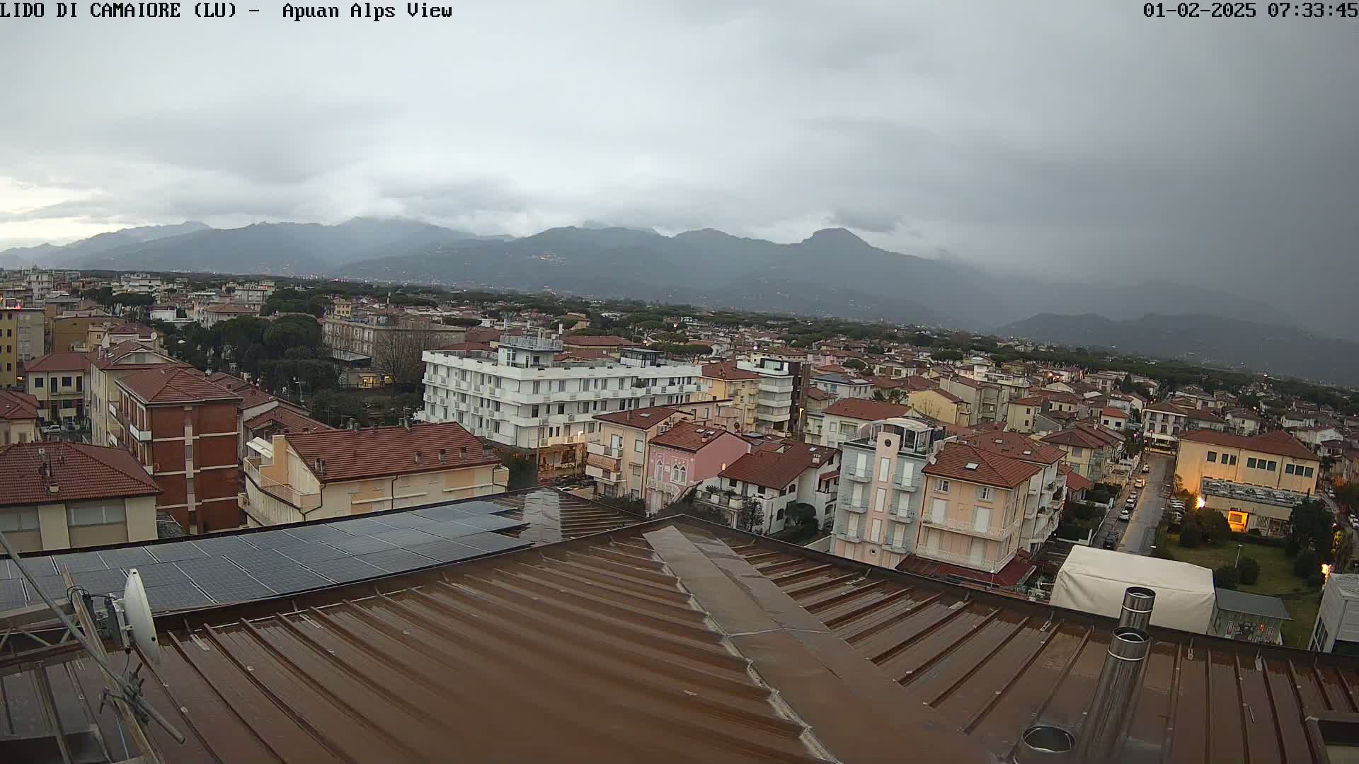 A wet brown roof overlooks a town nestled beneath overcast skies and distant mountains.