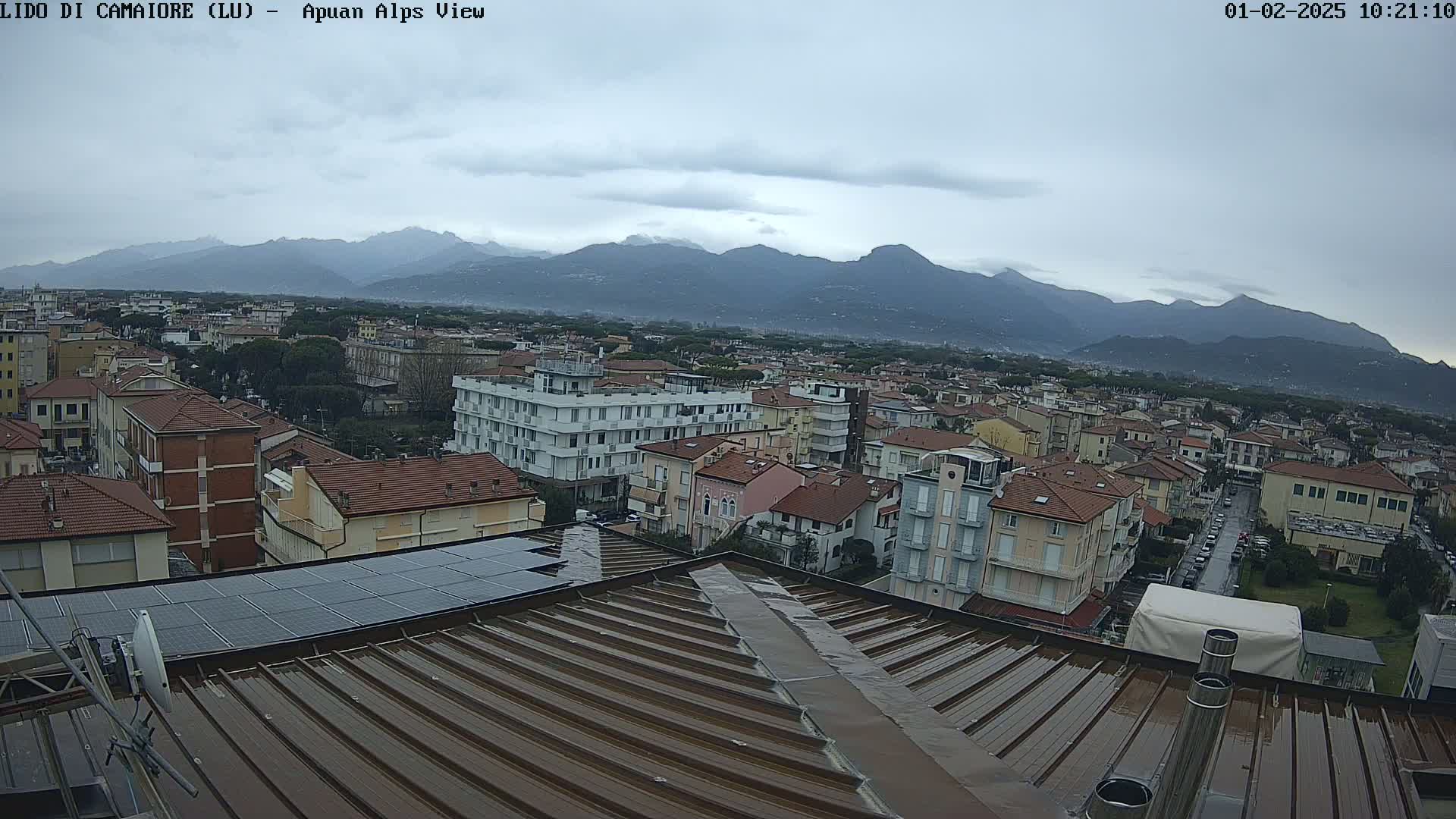 A wet rooftop overlooks a town nestled against a mountain range under an overcast sky.