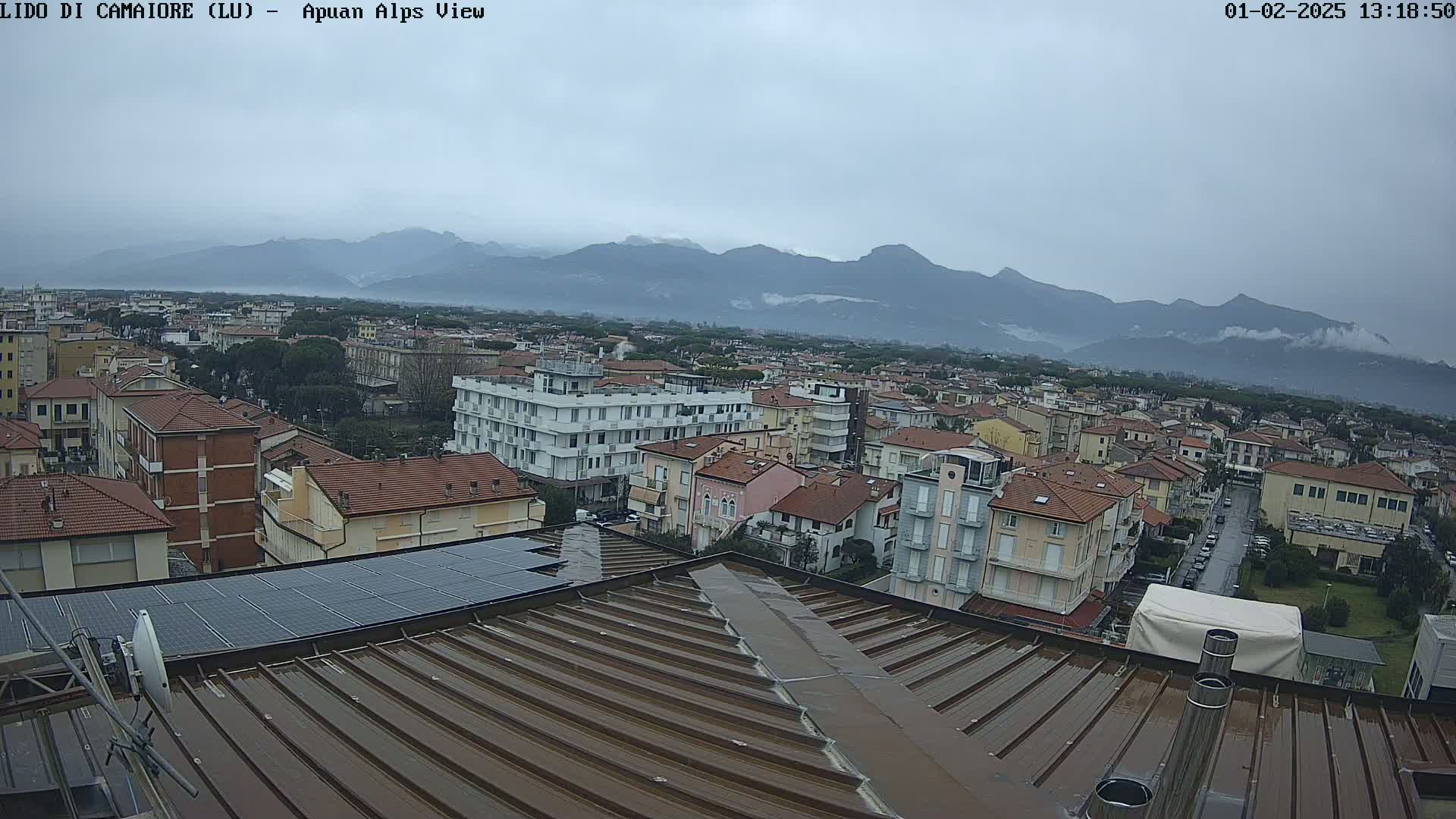 A wet rooftop overlooks a town nestled beneath a hazy mountain range on an overcast day.