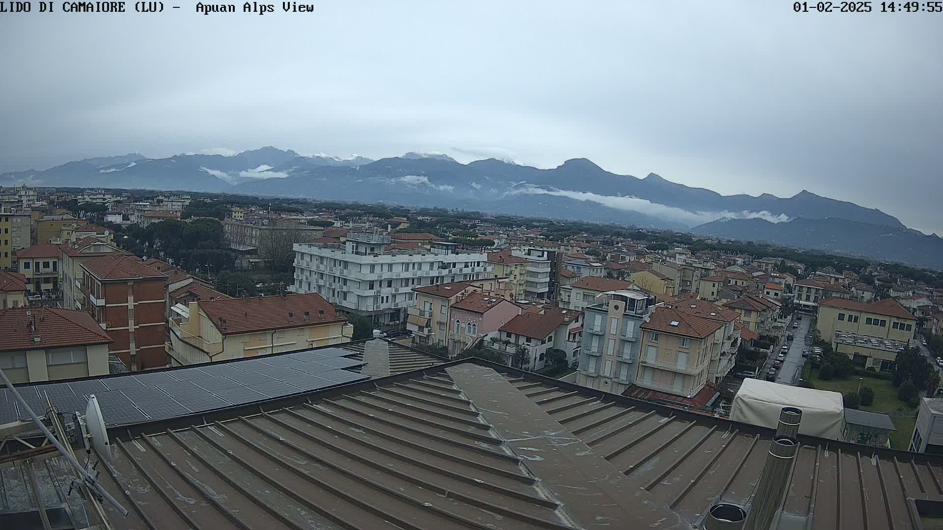 A view of a town with a flat, corrugated metal roof in the foreground, under a cloudy sky, with distant mountains partially obscured by fog or clouds.