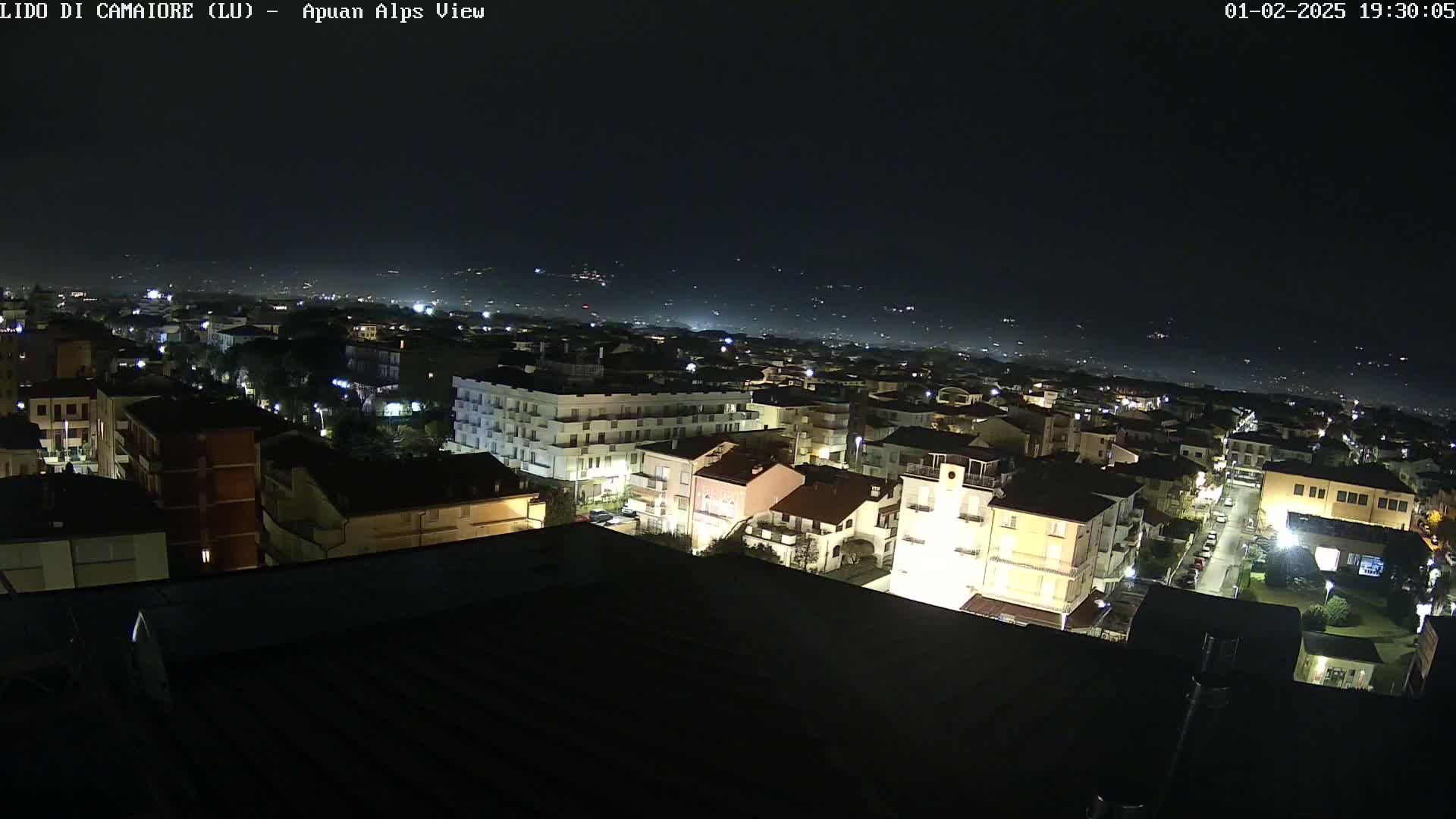 A nighttime, high-angle view of a town illuminated by streetlights, with a hazy, dark sky in the background.