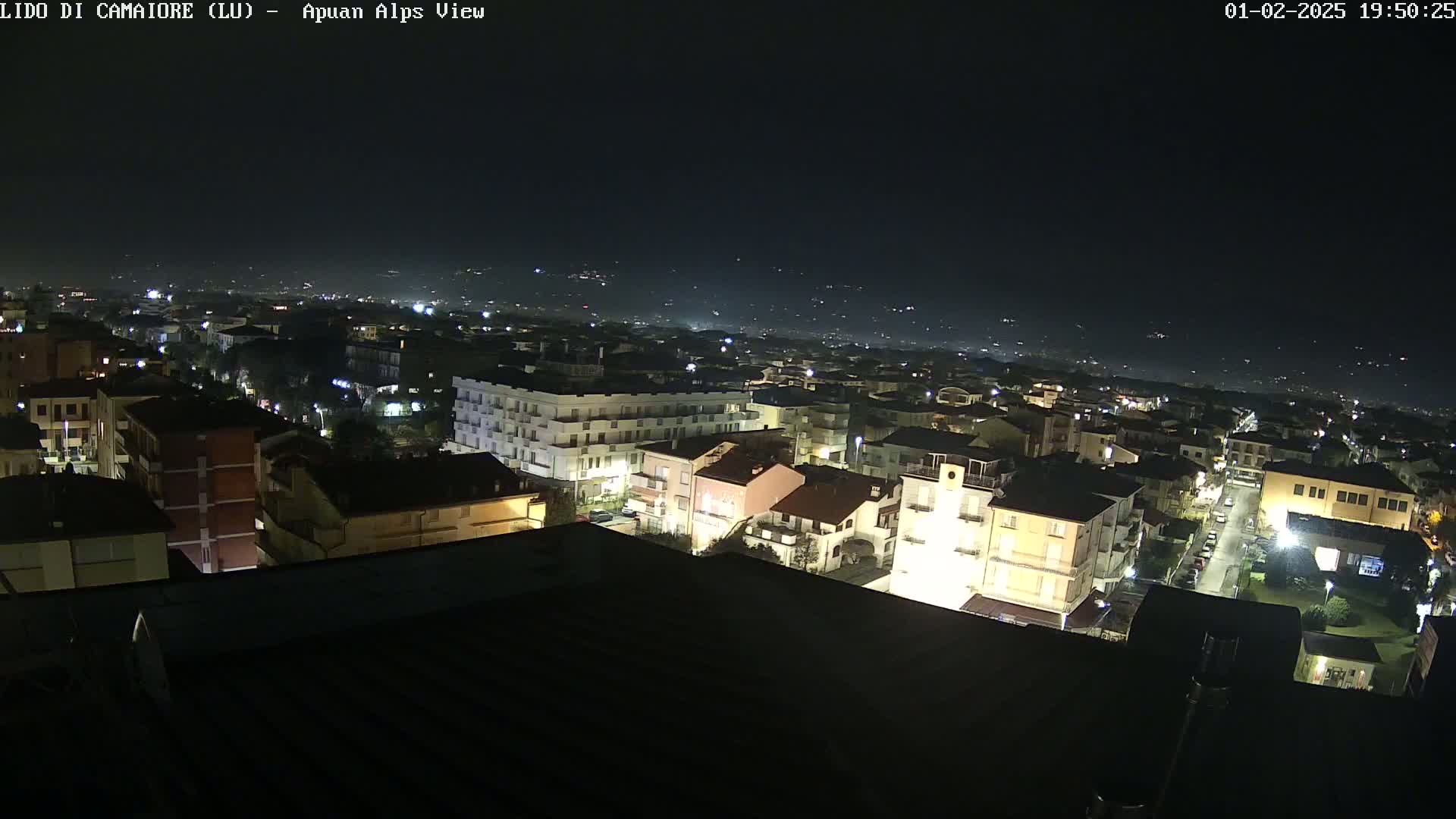 A nighttime aerial view of a town with illuminated buildings, streets, and distant lights under a dark, clear sky.