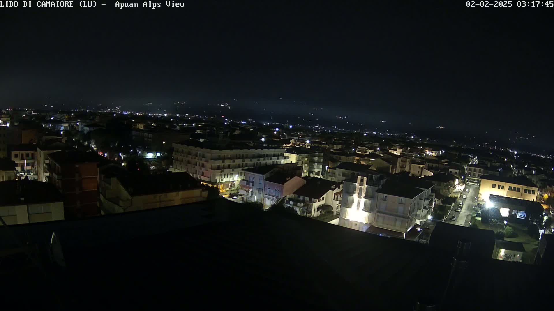 A nighttime aerial view shows a town illuminated by streetlights, with a dark, clear sky above.