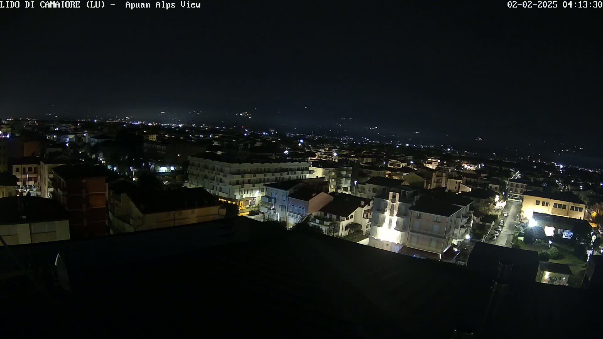 A nighttime, aerial view shows a town with dimly lit buildings and streets, extending to a dark, distant horizon under a clear, dark sky.