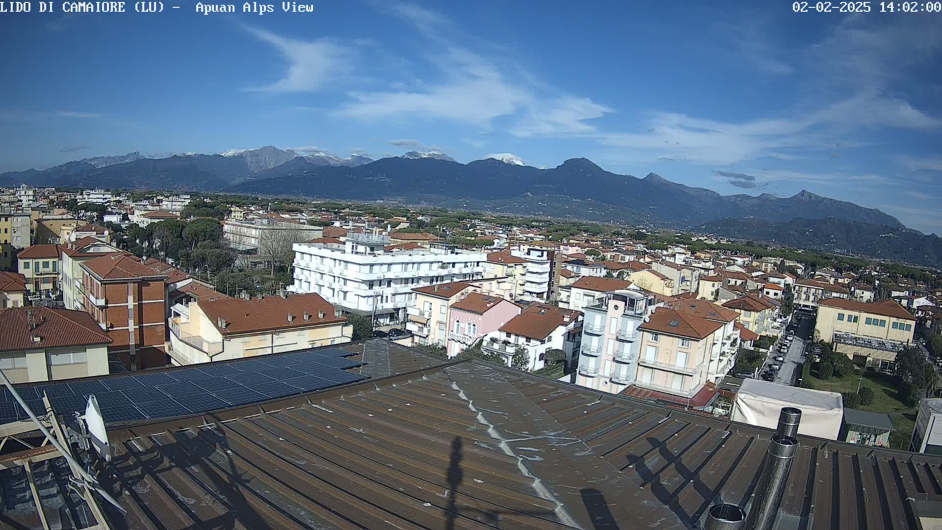 A rooftop view shows a town nestled against snow-capped mountains under a mostly clear blue sky.