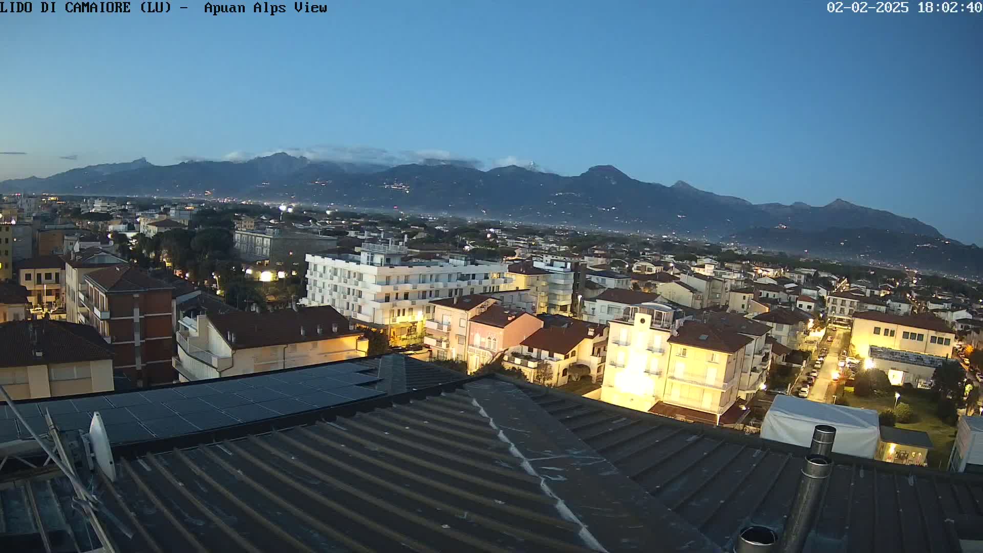 A nighttime view of a town nestled below a mountain range under a clear, twilight sky.