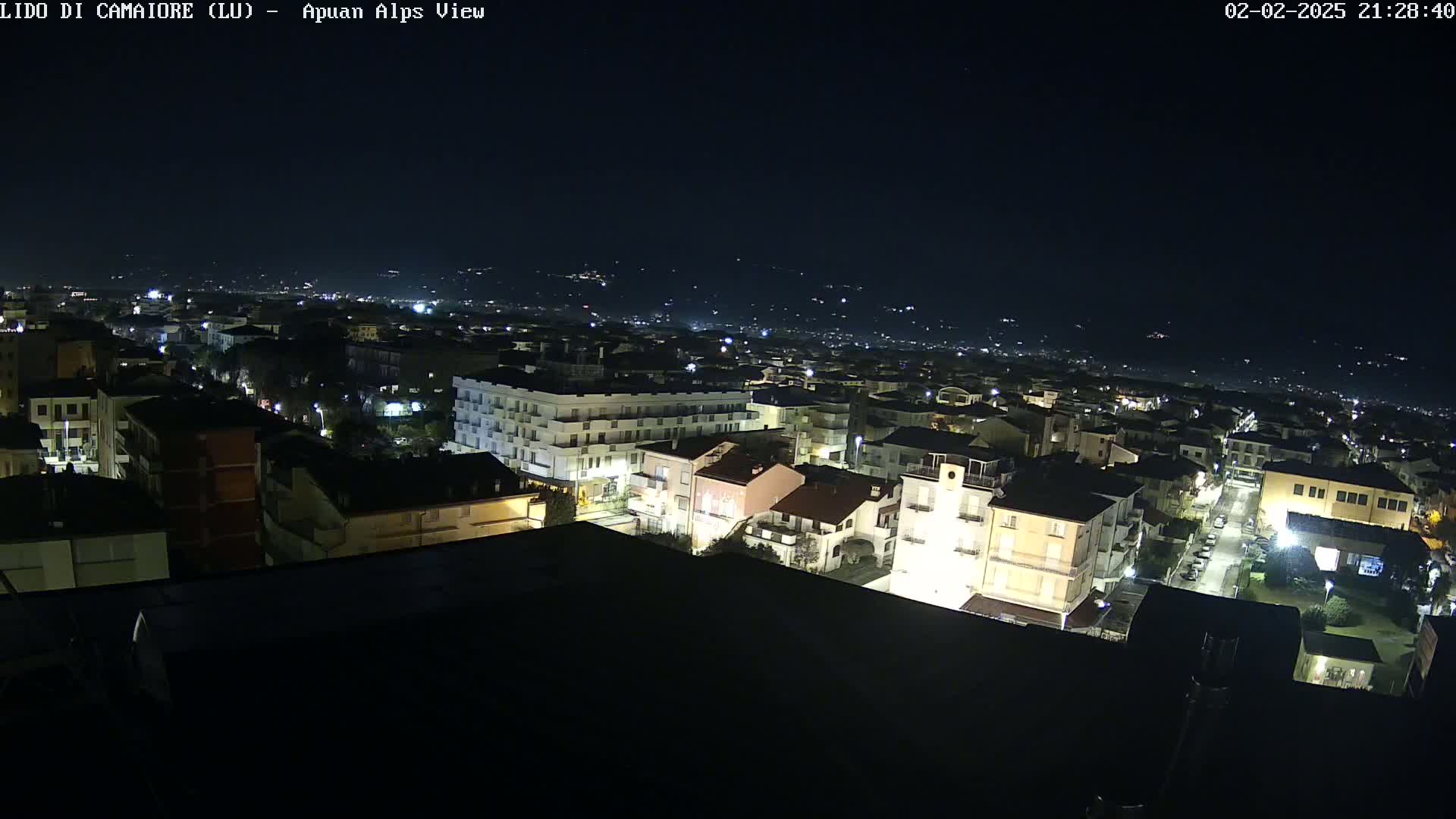 A nighttime aerial view of a town with dimly lit buildings and streets, under a clear, dark sky.