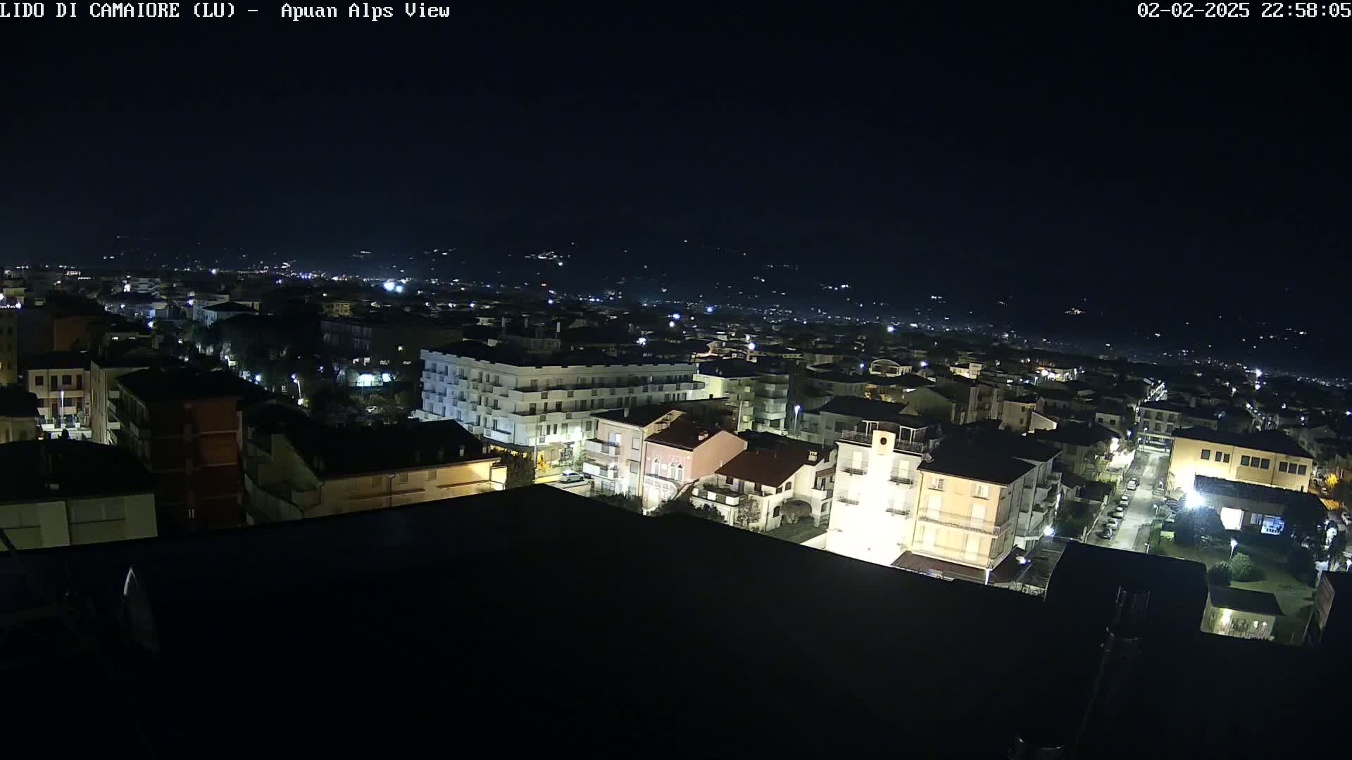 A nighttime, aerial view of a town shows numerous buildings illuminated by streetlights and other lights, under a clear, dark sky.