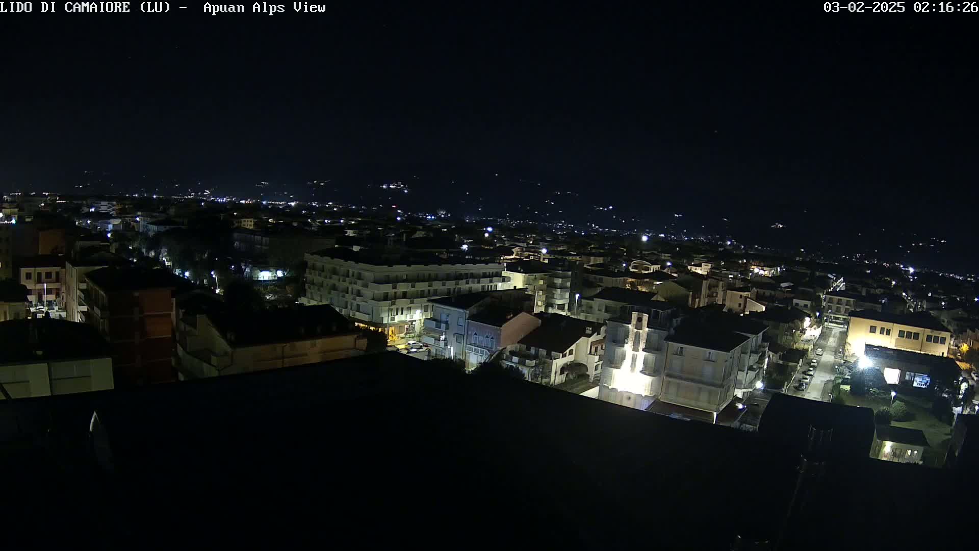 A nighttime aerial view of a town shows buildings illuminated by streetlights against a dark sky.