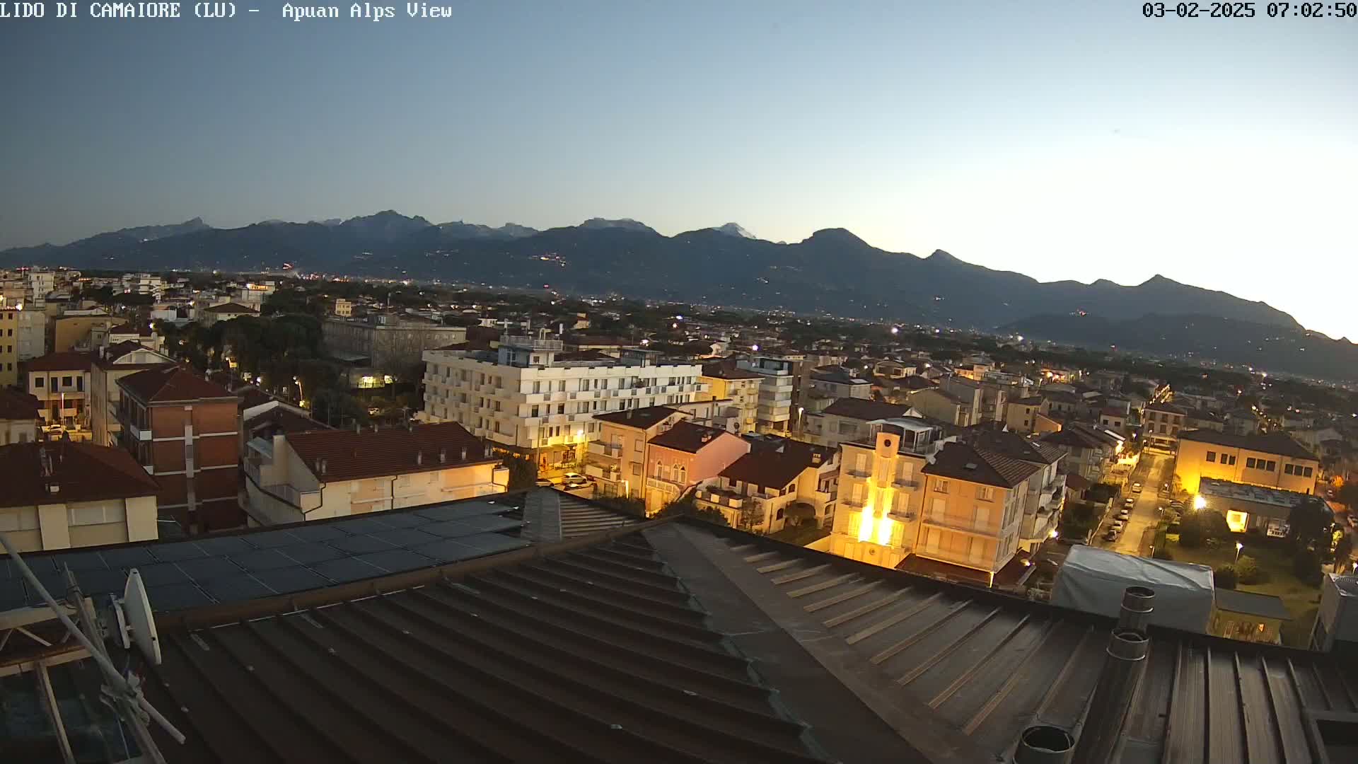 A twilight view of a town nestled beneath a mountain range, illuminated by streetlights.