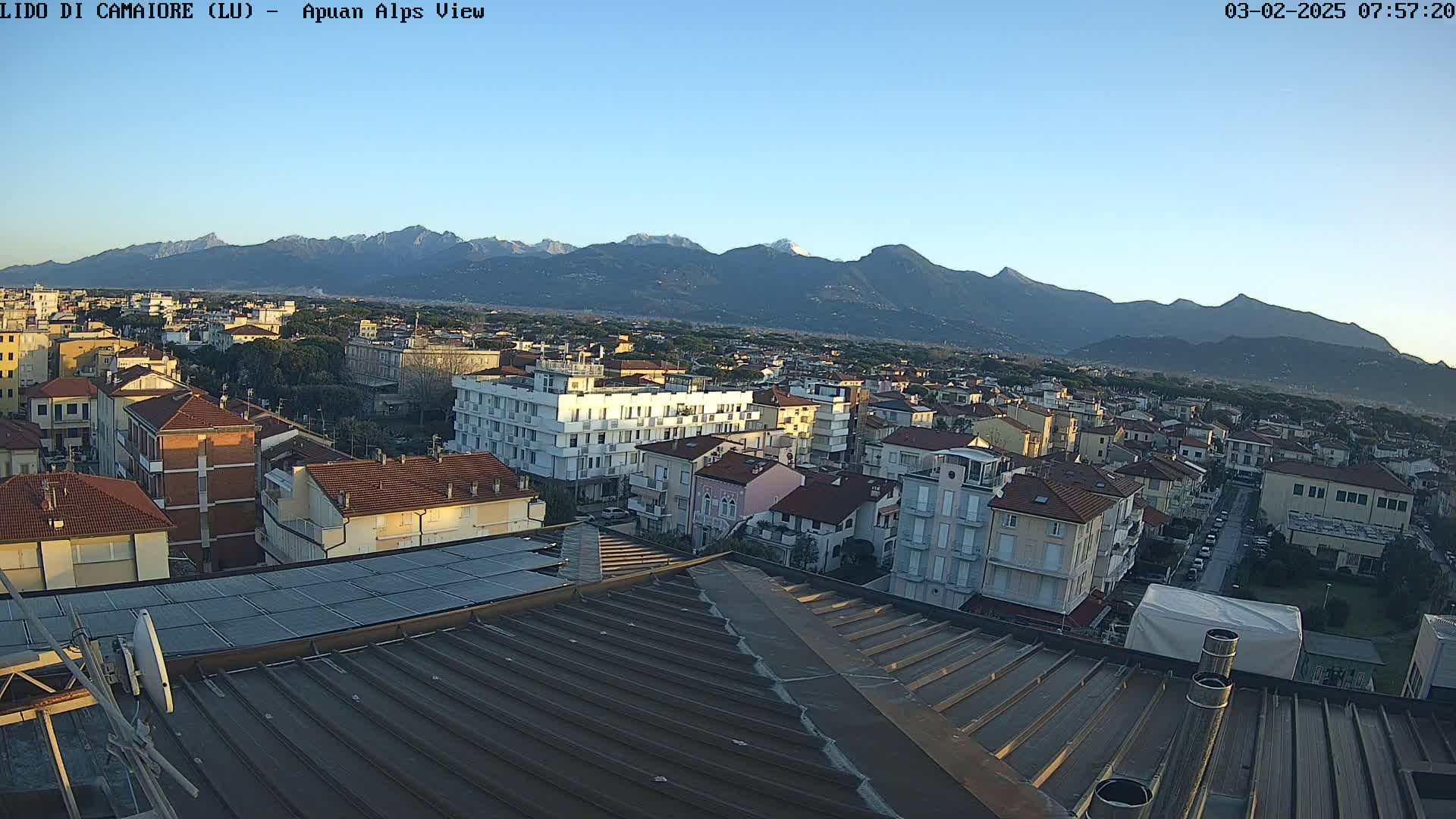 A rooftop view of a town shows a clear, sunny day with mountains in the background.