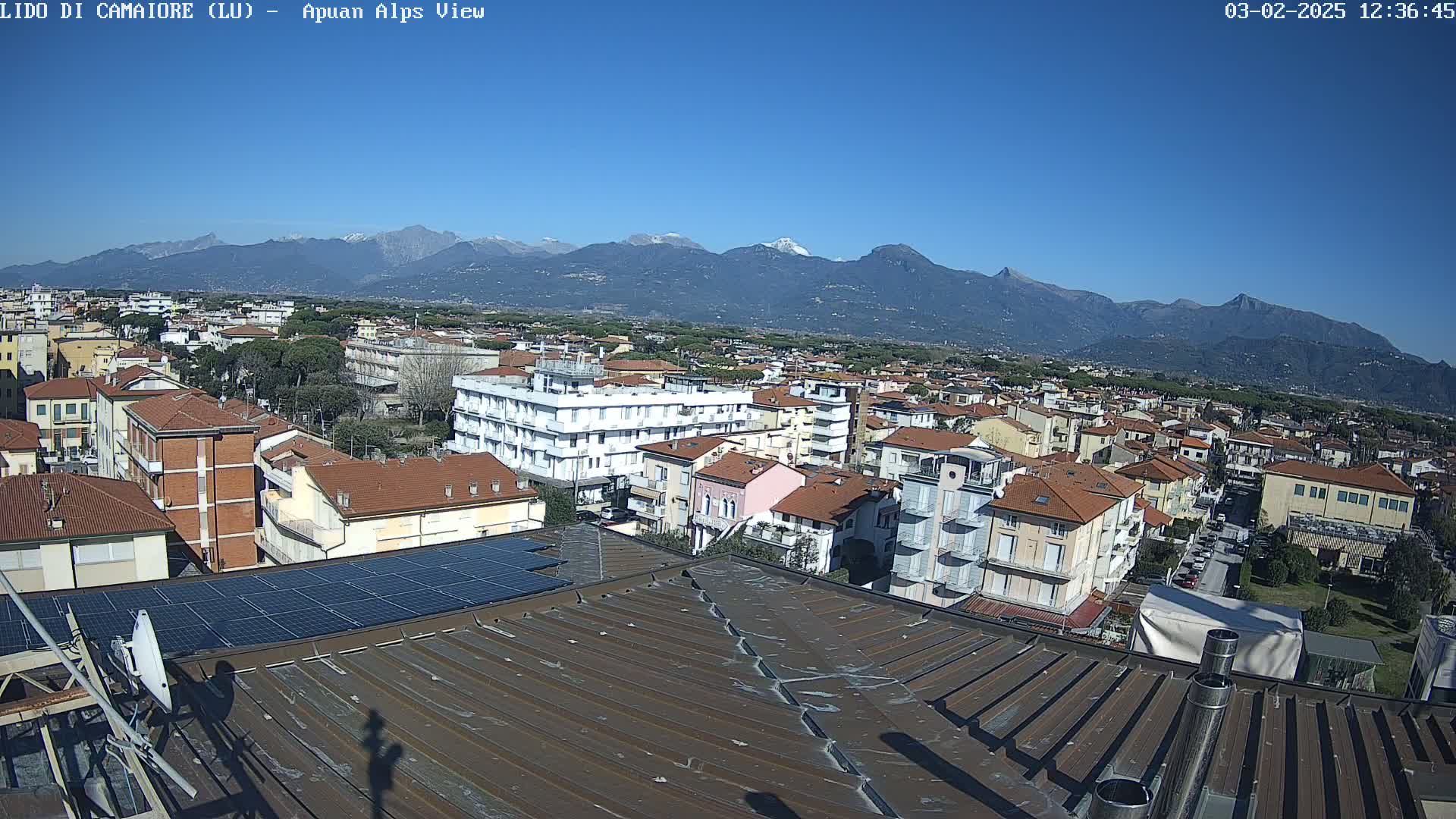 A rooftop view of a town nestled against a snow-capped mountain range under a clear blue sky.