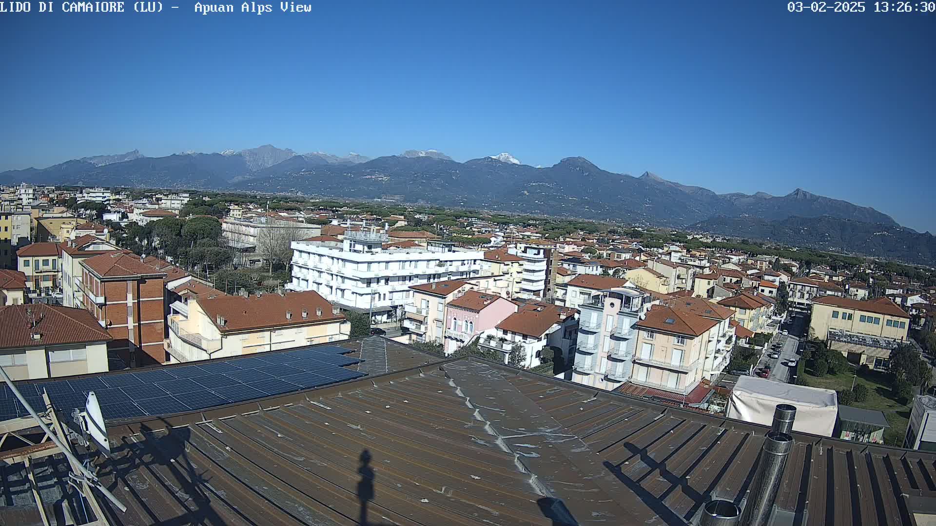 A rooftop view of a town on a clear, sunny day, with snow-capped mountains in the distance.
