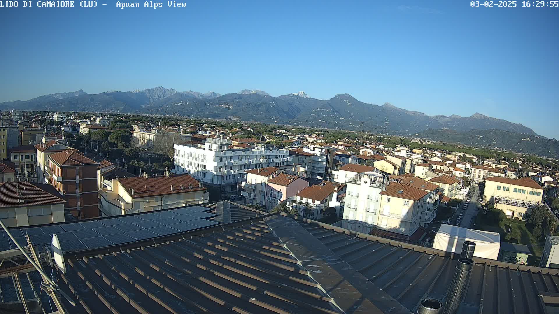 A rooftop view of a town nestled against a mountain range under a clear blue sky.
