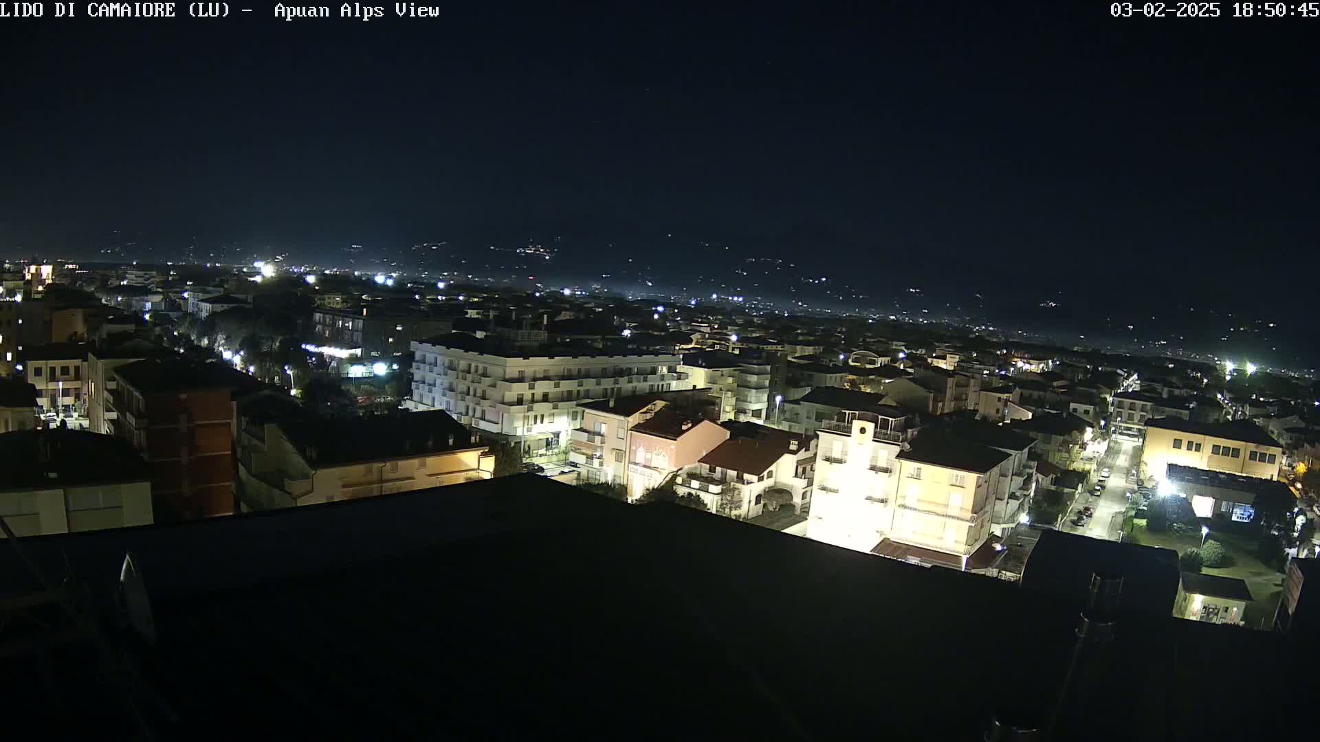 A nighttime aerial view of a town with streetlights illuminating buildings and roads, under a clear, dark sky.