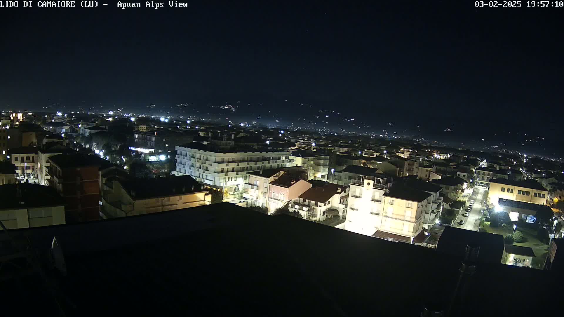 A nighttime aerial view of a town shows buildings illuminated against a dark sky.