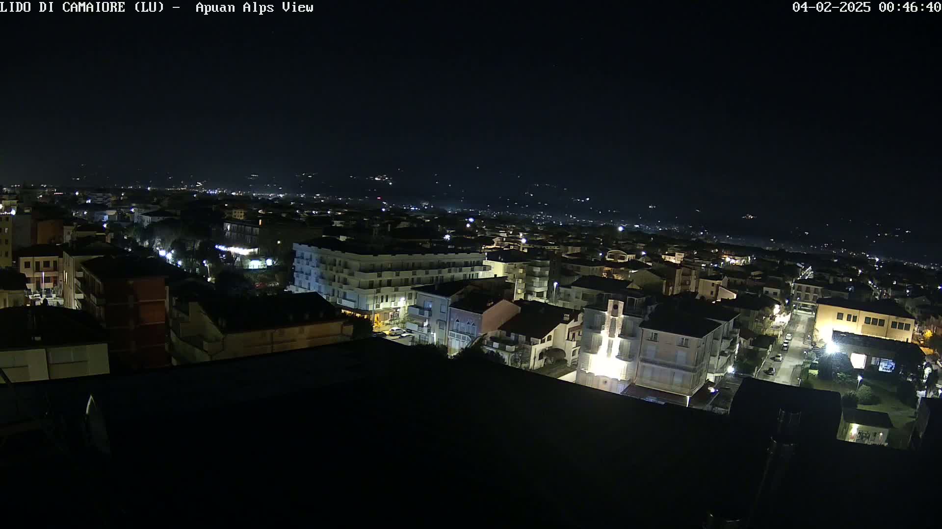 A nighttime aerial view shows a town illuminated by streetlights, with a dark, clear sky above.