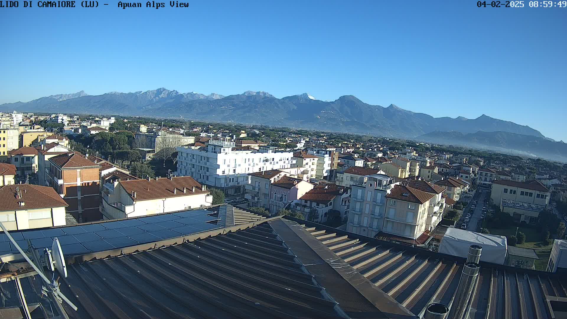 A rooftop view of a town nestled beneath a clear blue sky and a distant mountain range.