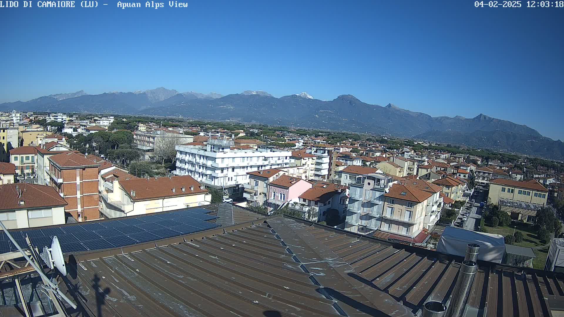 A rooftop view of a town on a clear, sunny day, with snow-capped mountains visible in the distance.