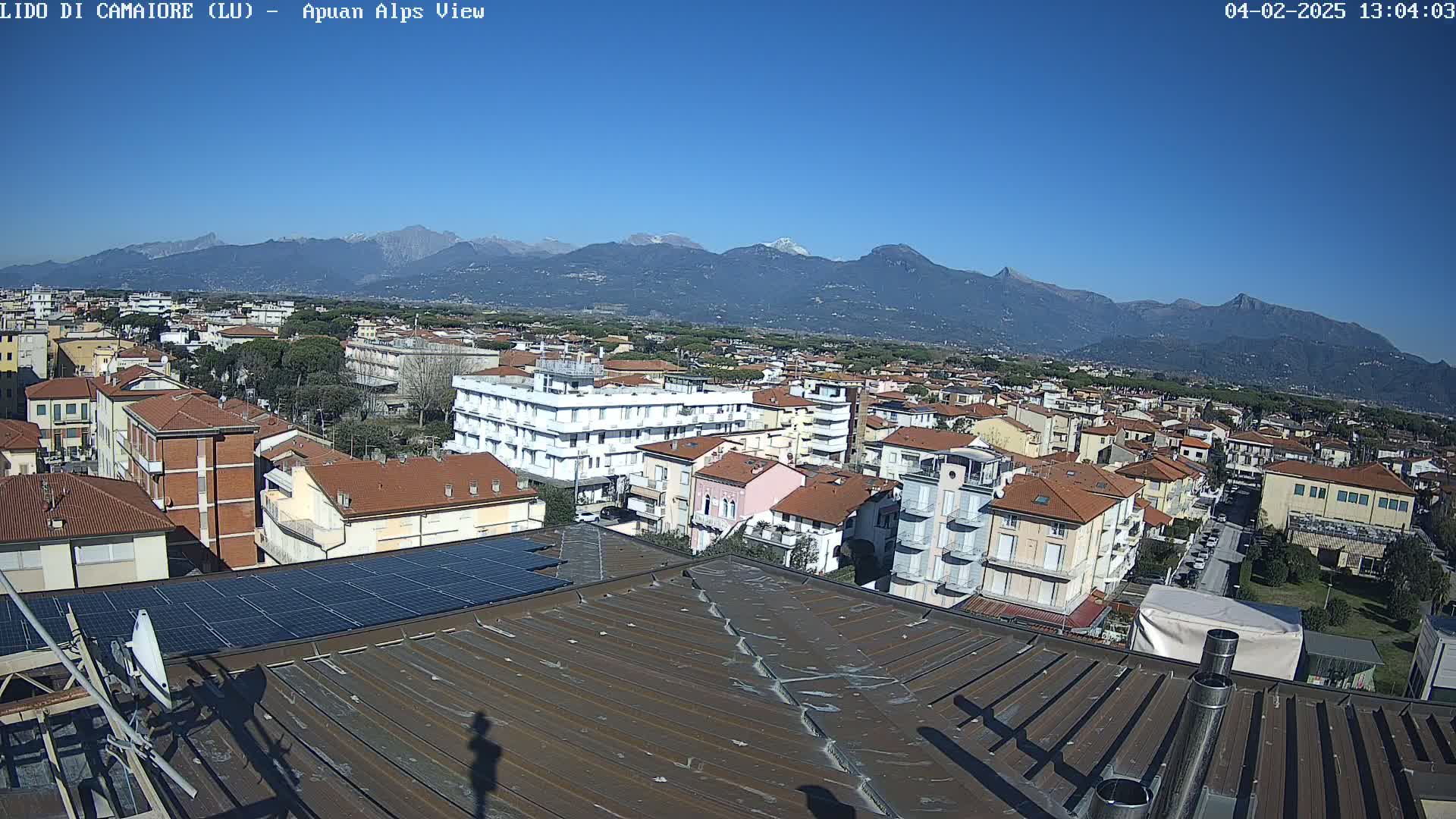 A rooftop view overlooking a town nestled against a mountain range under a clear blue sky.