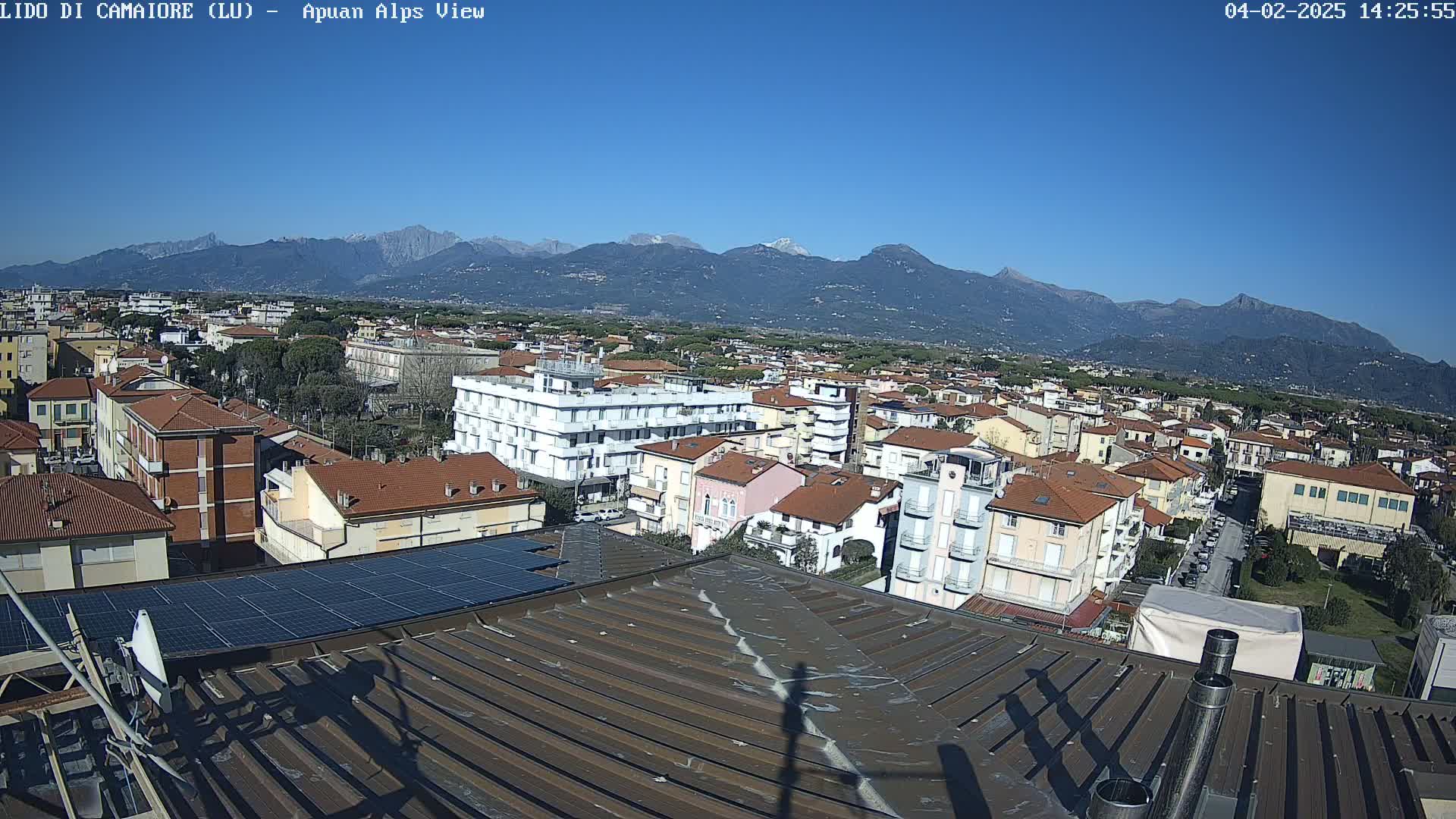 A rooftop view of a town nestled beneath a clear blue sky and snow-capped mountains in the distance.