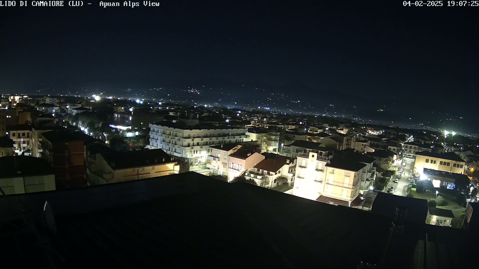 A nighttime, high-angle view of a town illuminated by streetlights, with a distant, dark mountain range visible under a clear sky.