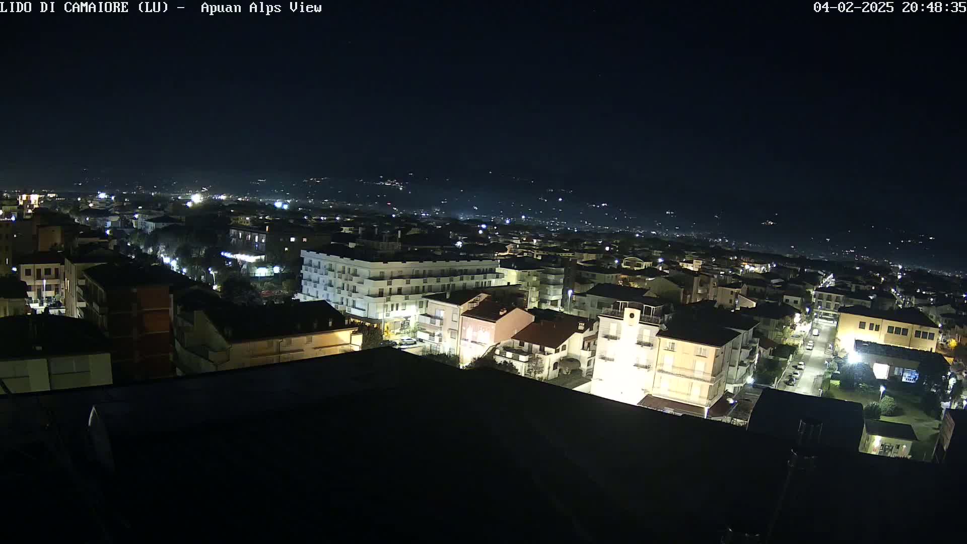 A nighttime, high-angle view of a town illuminated by streetlights, with distant lights suggesting other settlements under a clear, dark sky.