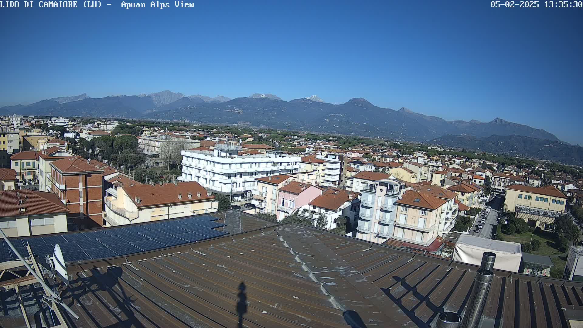 A rooftop view of a town nestled against a mountain range under a clear blue sky.