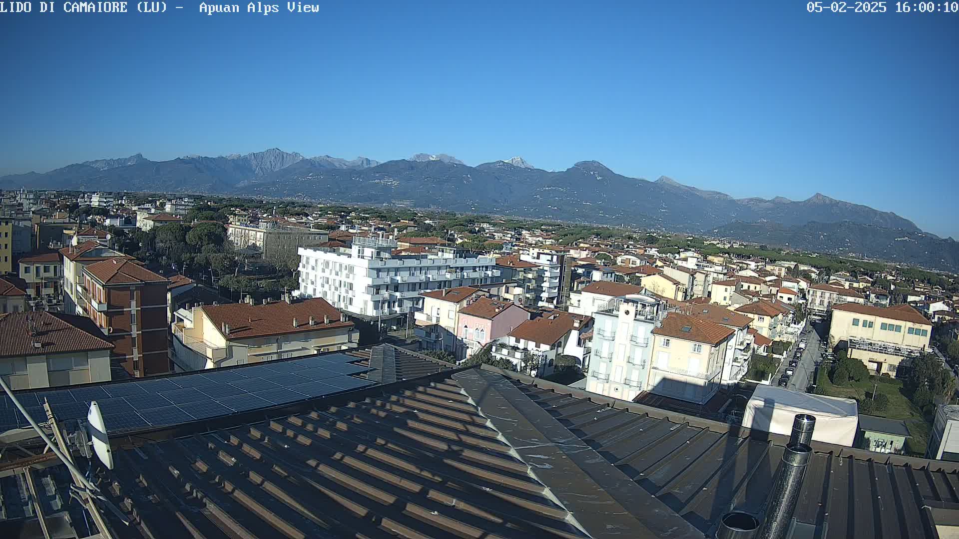 A rooftop view of a town nestled at the base of snow-capped mountains under a clear blue sky.