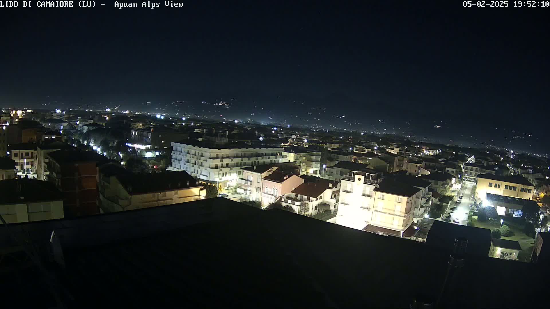 A nighttime aerial view of a town, illuminated by streetlights, with a dark, clear sky in the background.