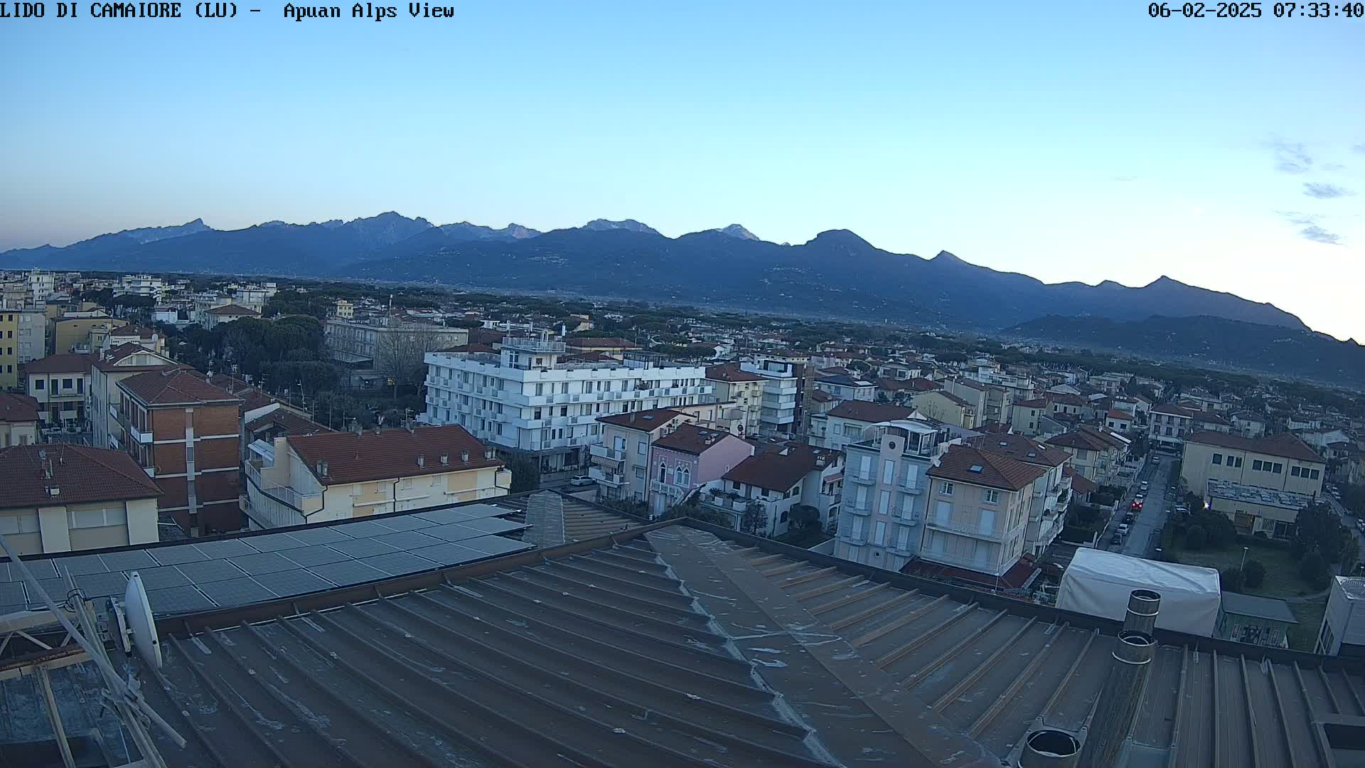 A high-angle view of a town under a clear, twilight sky, with a mountain range in the background.
