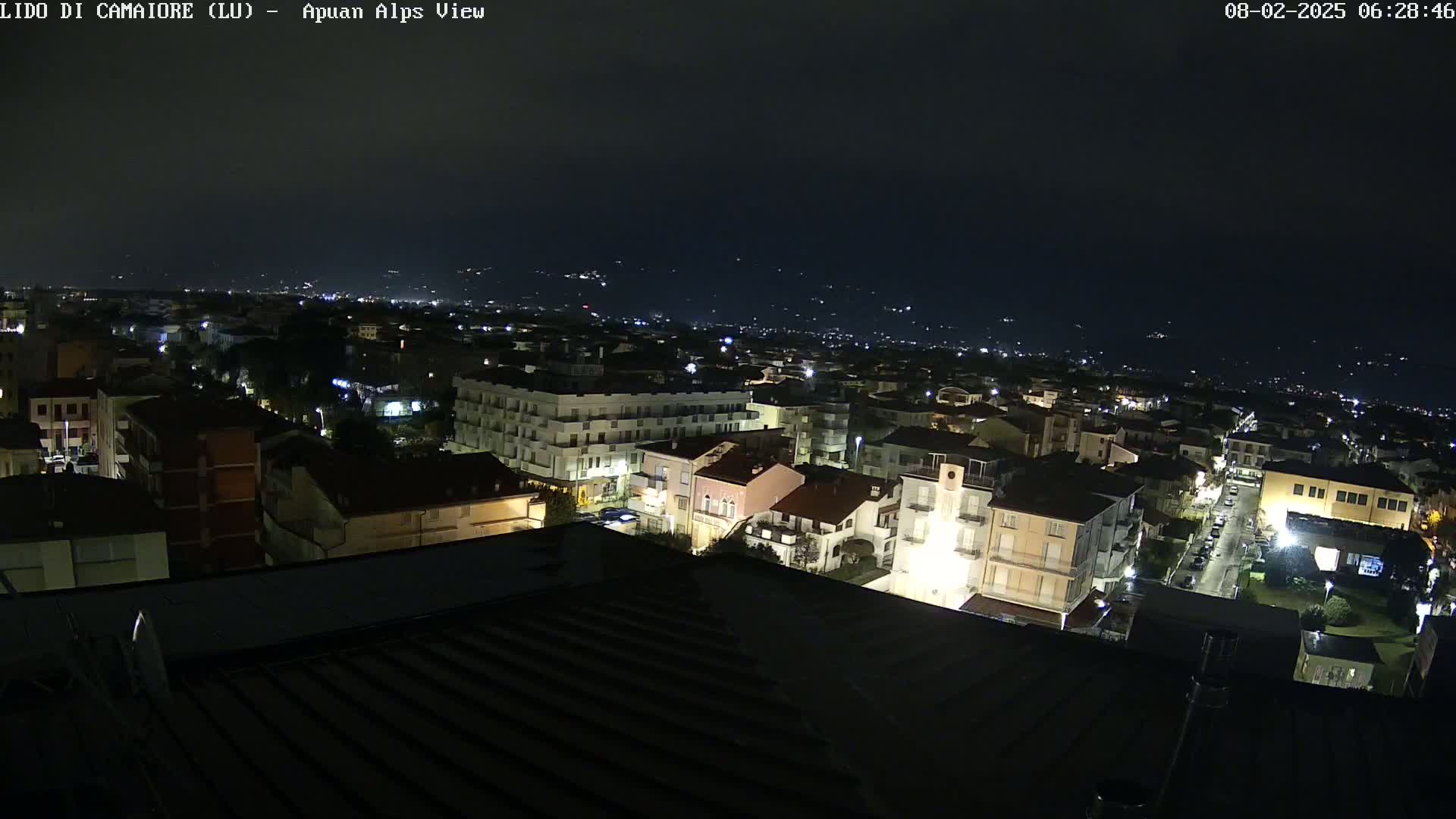 A nighttime aerial view of a town with dimly lit buildings and streets, under a dark, clear sky.