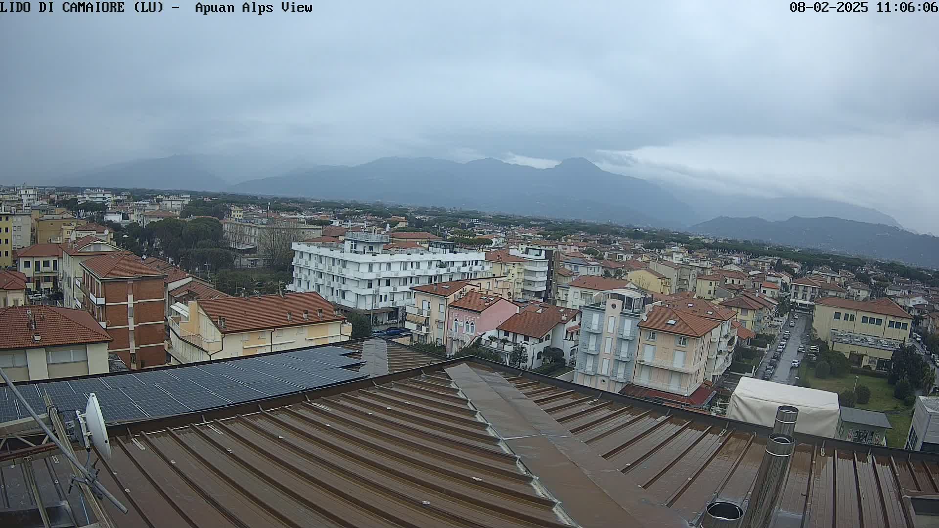 A rooftop view of a town under an overcast sky, with mountains visible in the distance.
