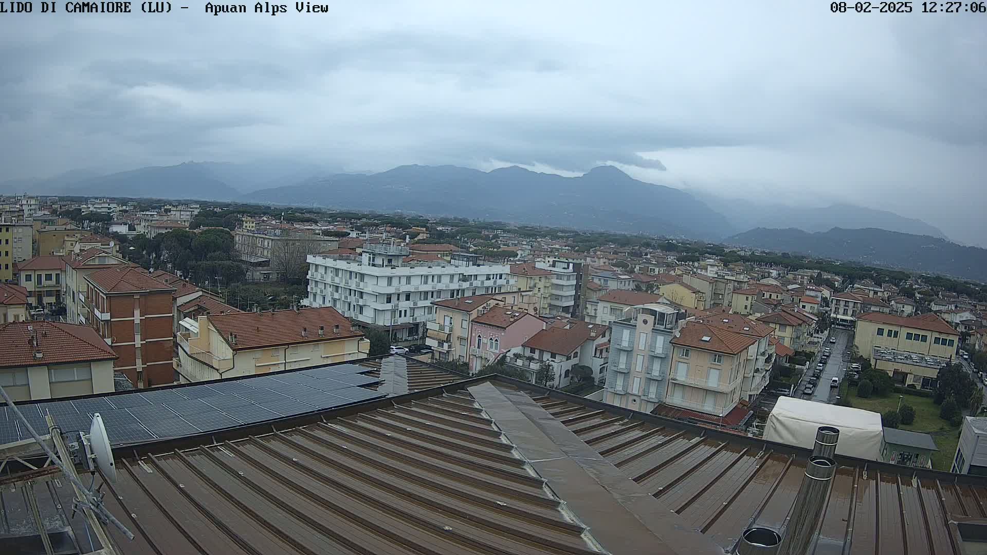 A rain-slicked rooftop overlooks a town nestled against a range of mountains under an overcast sky.
